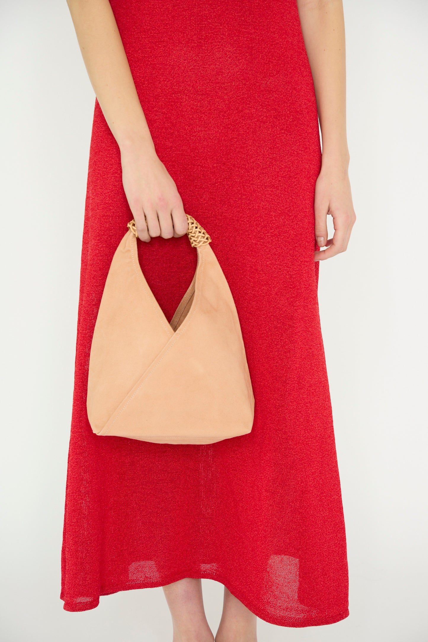 A person in a red dress stands against a light background, holding the Woven Triangle Bag 38 in Pink and Natural by Kamaro'an, featuring a woven canvas handle.