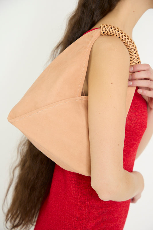 A woman in a red dress carries the Kamaro'an Woven Triangle Bag 38 in Pink and Natural, featuring a woven canvas strap, over her shoulder.