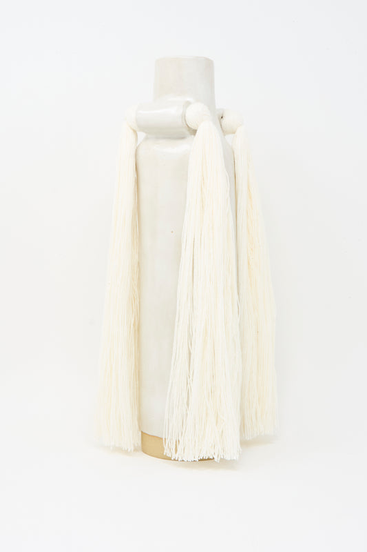 Vase #703 in White by Karen Tinney, a tall handmade stoneware vase with long, thick off-white yarn fringe draped from its sides, is shown against a plain white background.