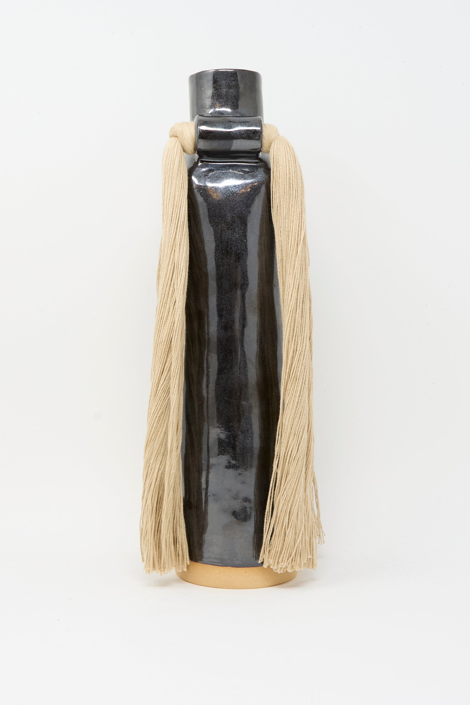 Vase #703 in Black by Karen Tinney is a tall, handmade stoneware vase with a glossy black glaze, cylindrical form, beige base, and long beige yarn elegantly draped from each side of the neck.