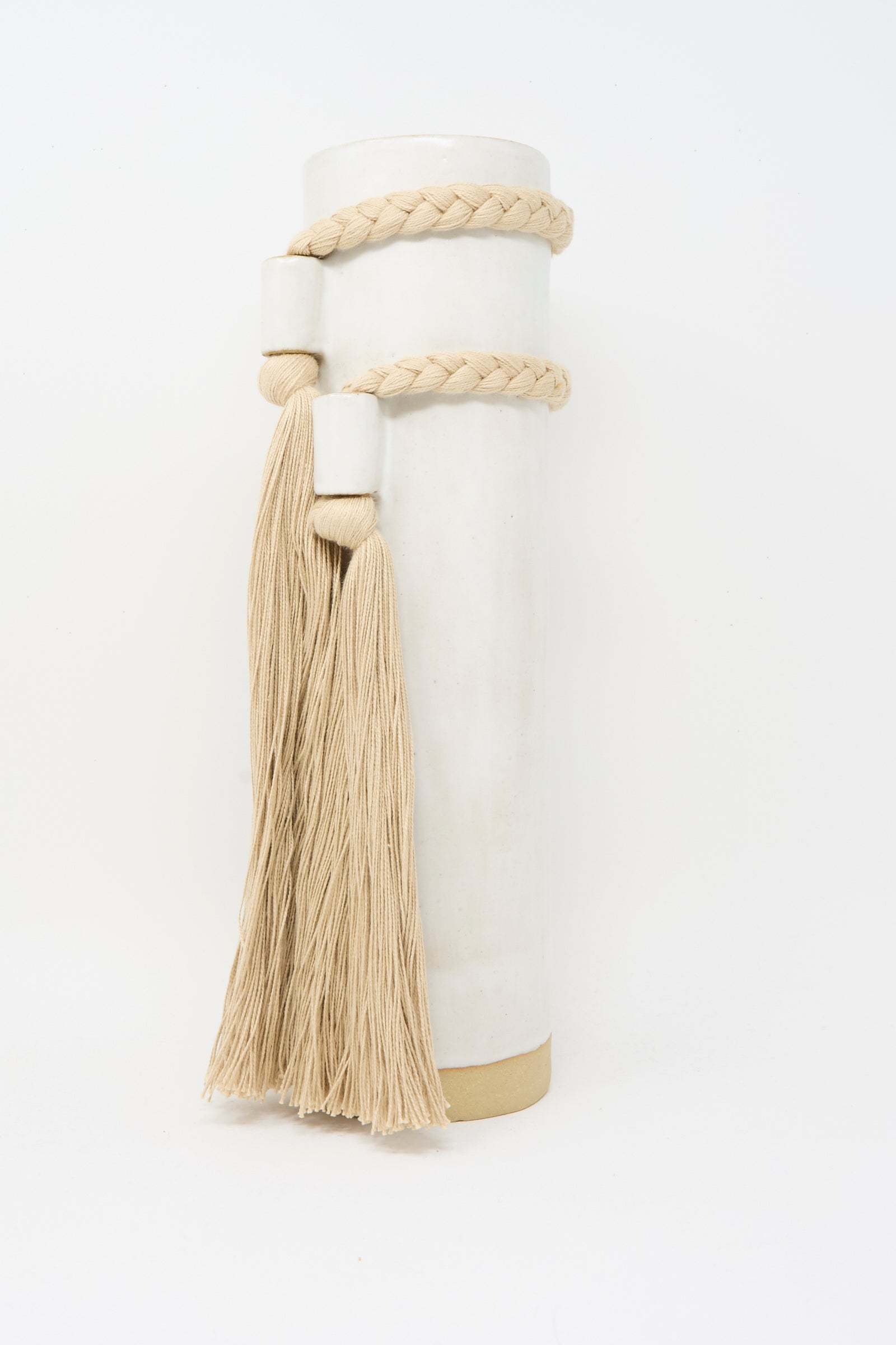 Karen Tinney's Vase #735 in White is a tall, handmade piece featuring a beige braided rope with two long tassels around its upper half, displayed against a plain white background.