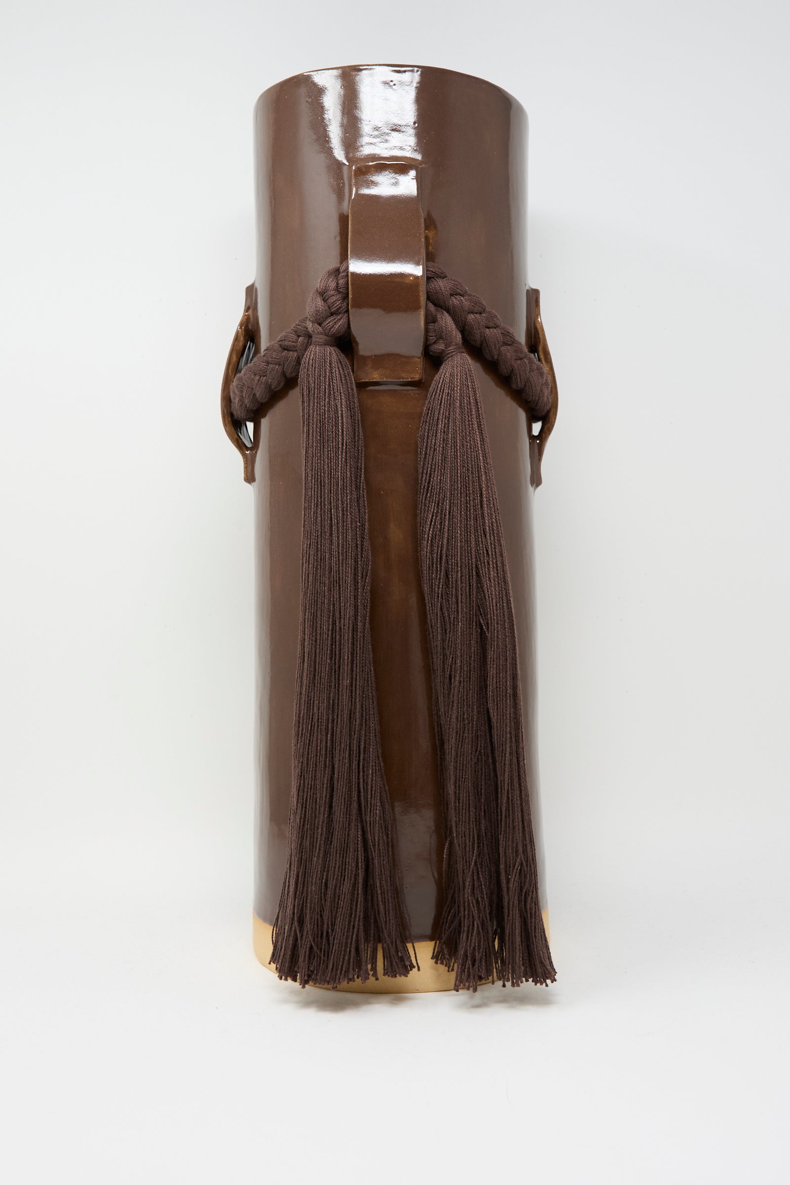 The Karen Tinney Vase #800 in Brown is a tall, glossy handmade Vermont vase with a central handle, braided rope accents, and two long brown tassels on the front.
