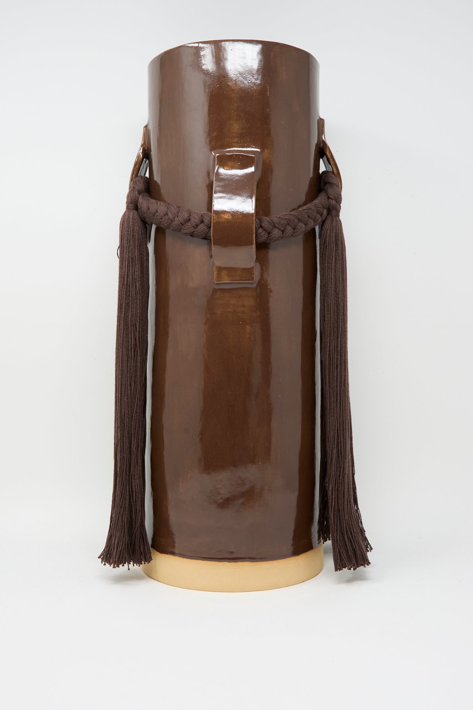 The Karen Tinney Vase #800 in Brown features a tall, cylindrical shape, a rectangular handle, braided cord, and two long tassels on each side—handmade in Vermont for a timeless touch.