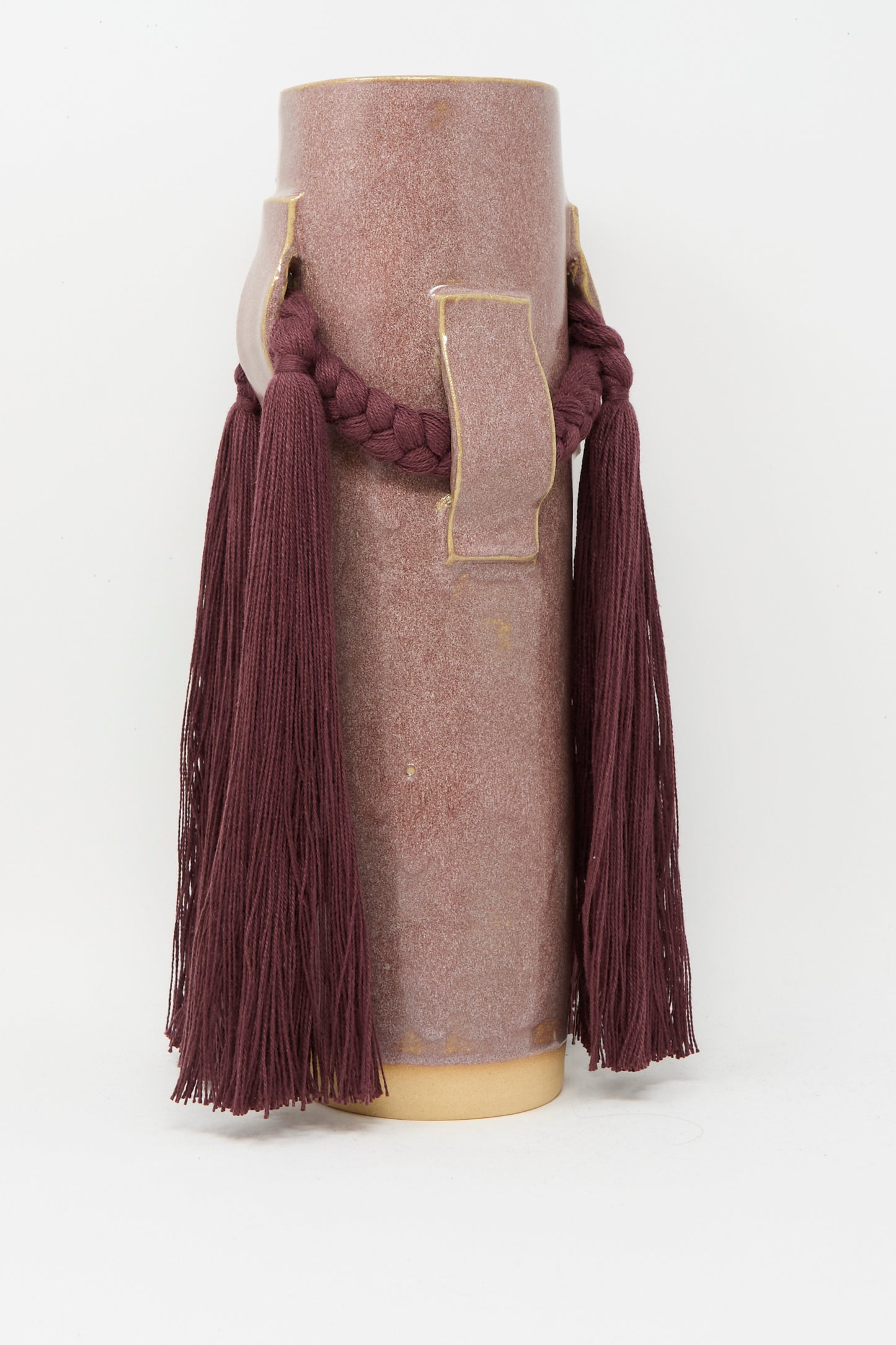 Karen Tinney’s Vase #800 in Burgundy is a tall ceramic stoneware vase with a matte mauve finish, adorned with braided burgundy cord and long matching tassels for a modern take inspired by classic Vermont pottery.