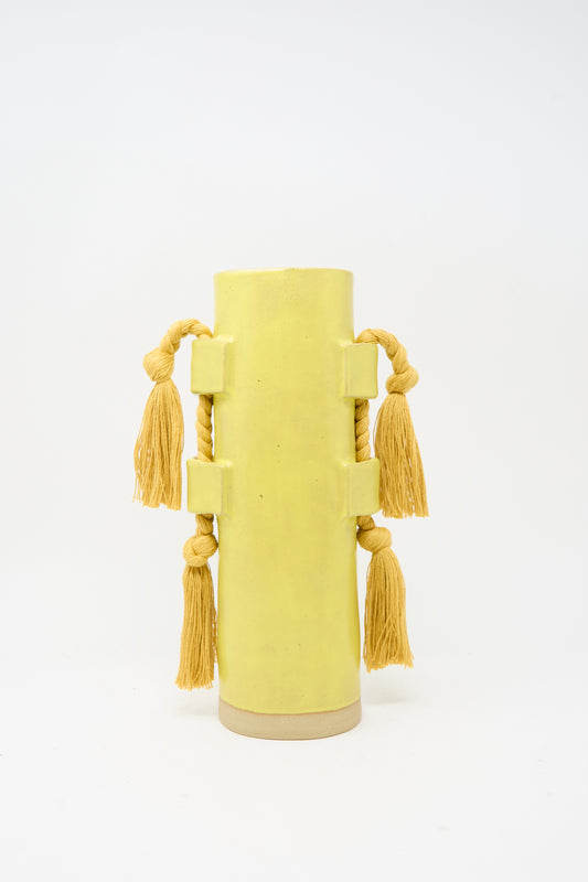 Vase #504 in Marigold by Karen Tinney is a tall, cylindrical vessel featuring four thick rope handles, each accented with a large yellow tassel. Set against a plain white background, this handmade piece adds artisan charm to any space.