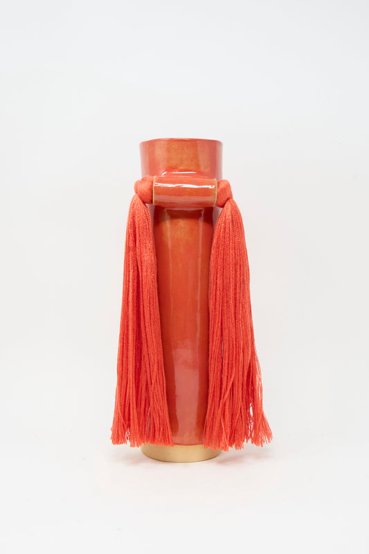 Vase #531 in Red by Karen Tinney is a handmade stoneware vase, expertly crafted in the spirit of Vermont pottery. This tall, glossy red ceramic piece features two long tassels hanging from a horizontal bar near the top and is set against a white background.