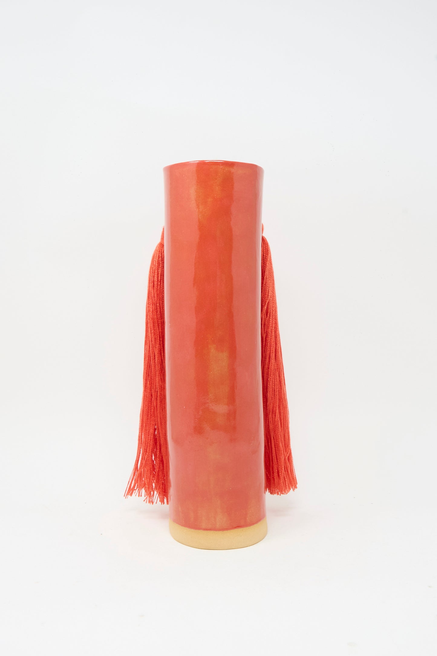 Vase #531 in Red by Karen Tinney is a tall, cylindrical red ceramic vase featuring long red tassels on each side.