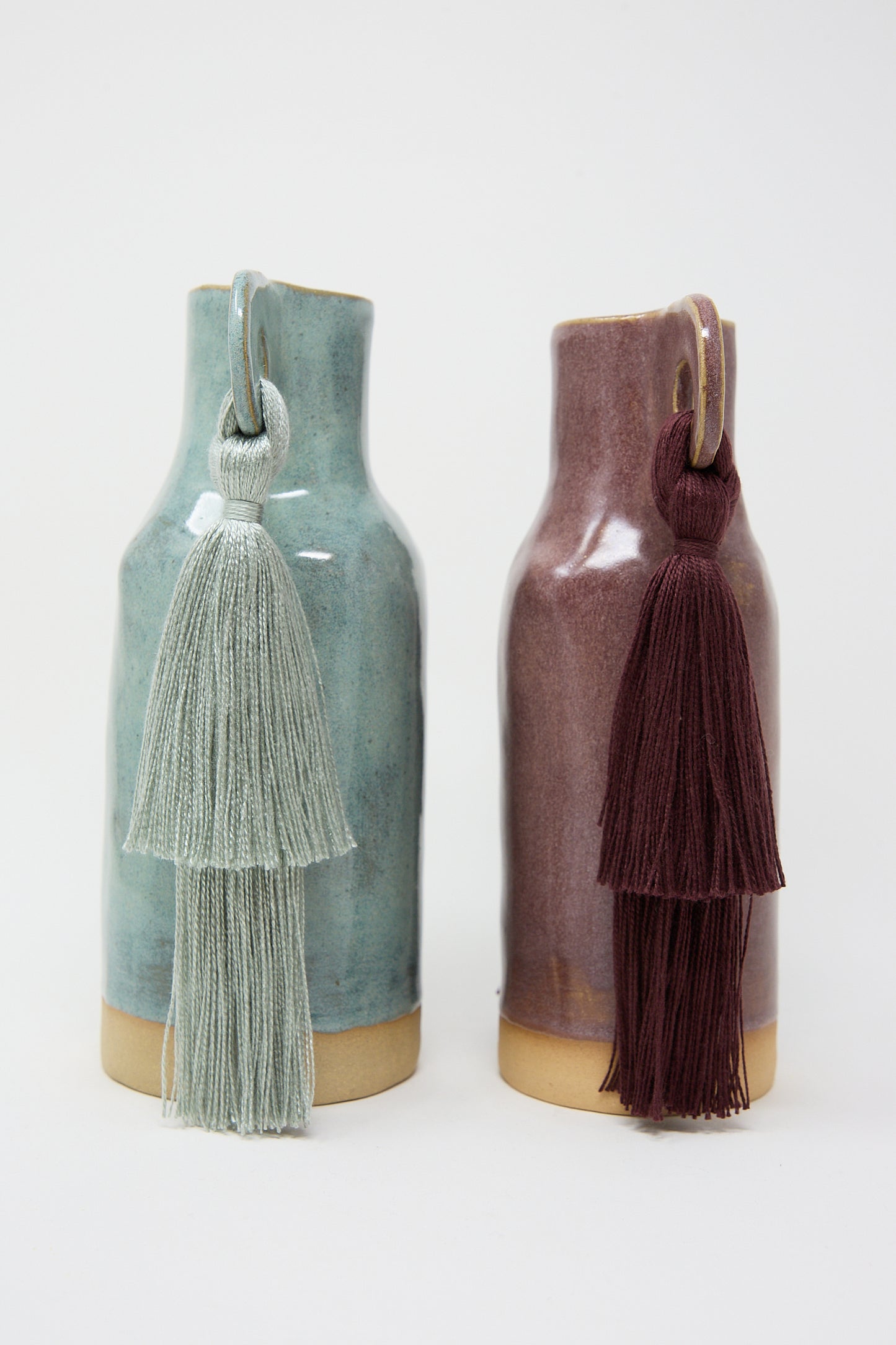 Two Karen Tinney handmade ceramic bottles with tassels on a white background.
