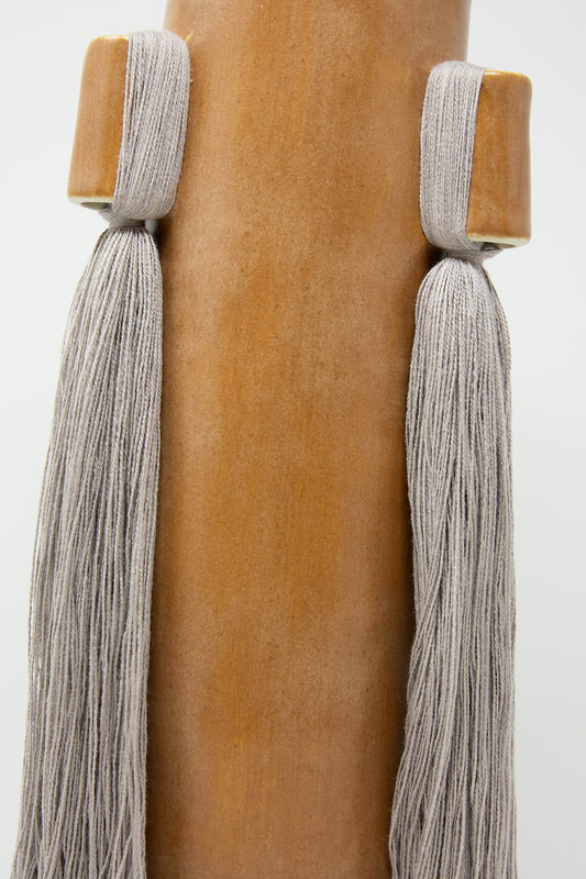 Close-up of tassels hanging on a post with a smooth, handcrafted Karen Tinney Vase #607 in Brown surface.