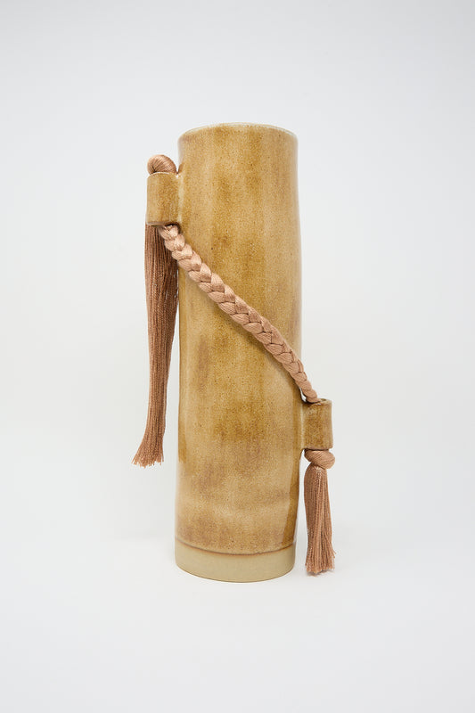 Karen Tinney's Vase #695 in Amber leather cylindrical case with braided strap and tassels against a white background, featuring an amber brown glaze.