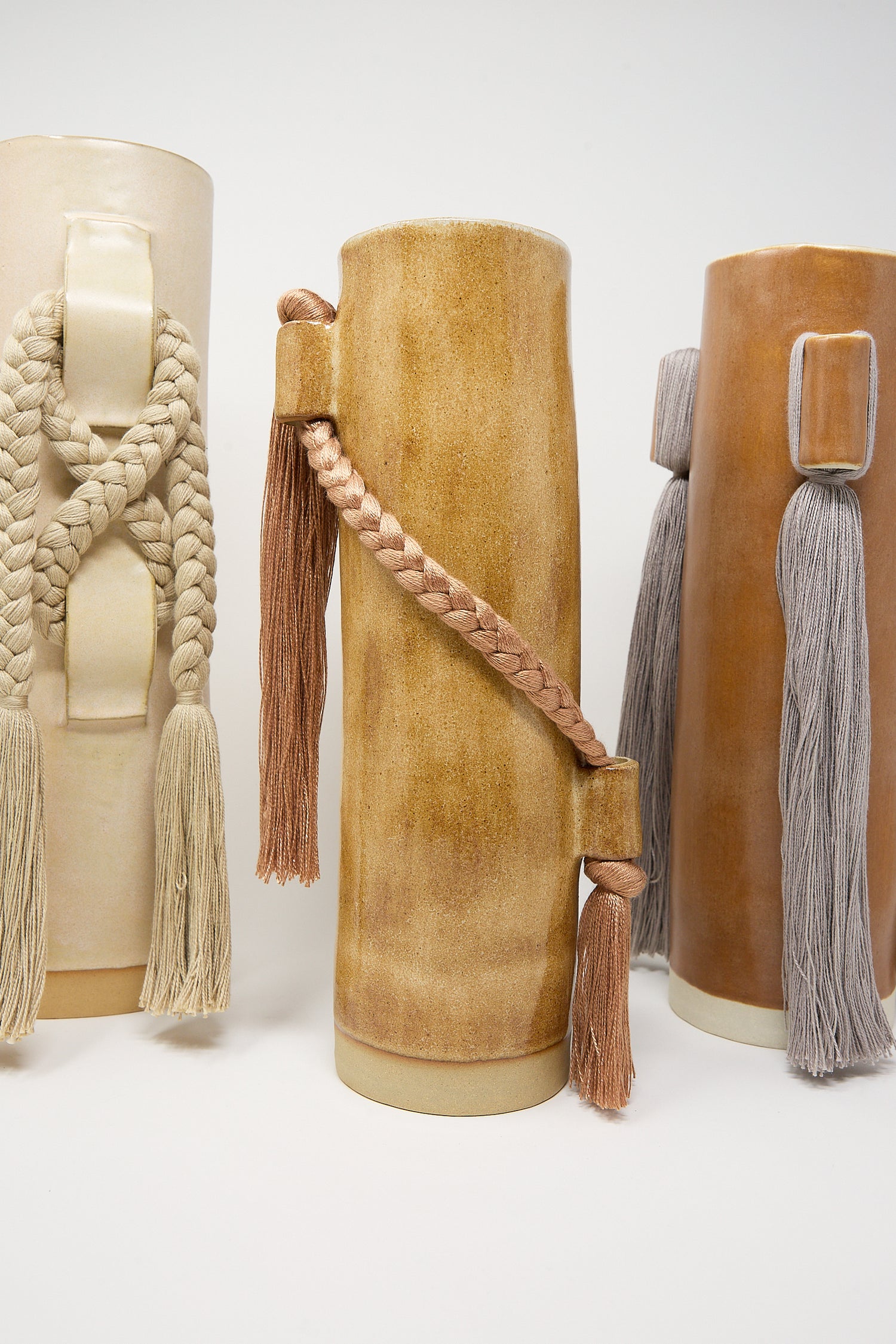 Three cylindrical leather containers with decorative tassels and braided details on a white background are displayed beside a Karen Tinney Vase #695 in Blue.