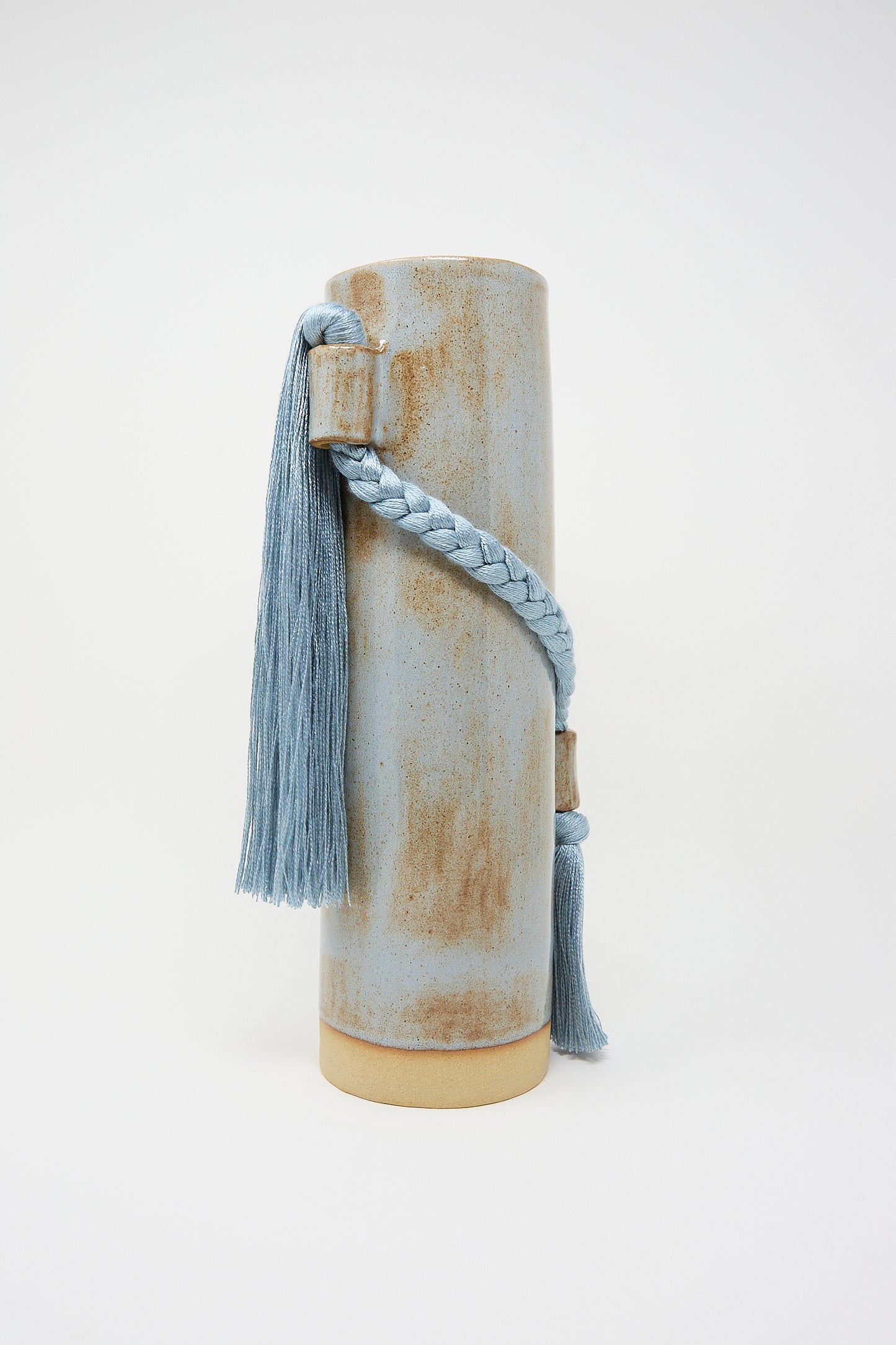 A Karen Tinney stoneware Vase #695 in Blue with a tassel attached to its side on a white background.