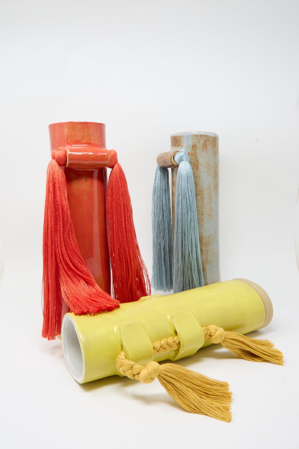Three cylindrical vases by Karen Tinney, each crafted by hand in stoneware and finished with a satin tan glaze, are displayed on a plain white background. 