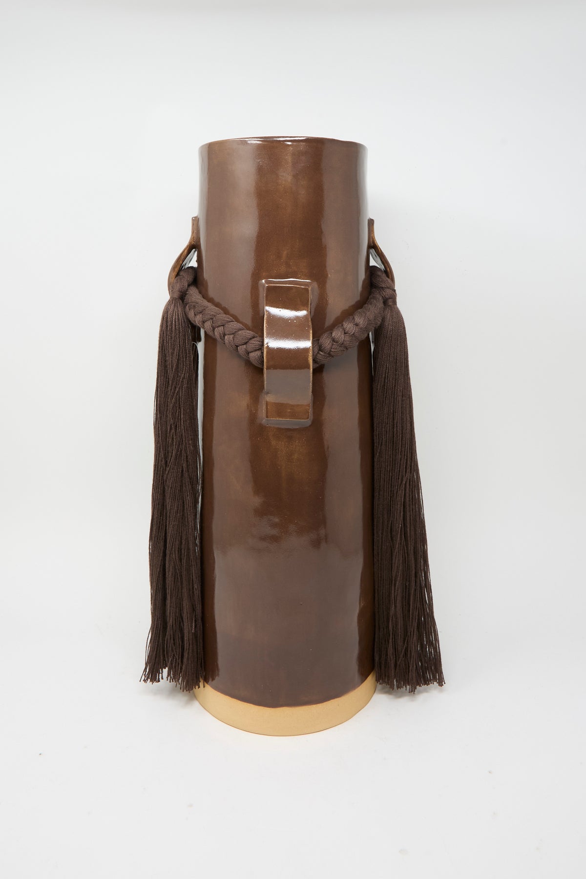 Vase #800 in Brown by Karen Tinney features a tall, glossy brown glazed form with a central handle, thick braided rope adorned with long tassels on each side, and stands on a cream-colored base—a striking example of the brand’s Vermont pottery craftsmanship.