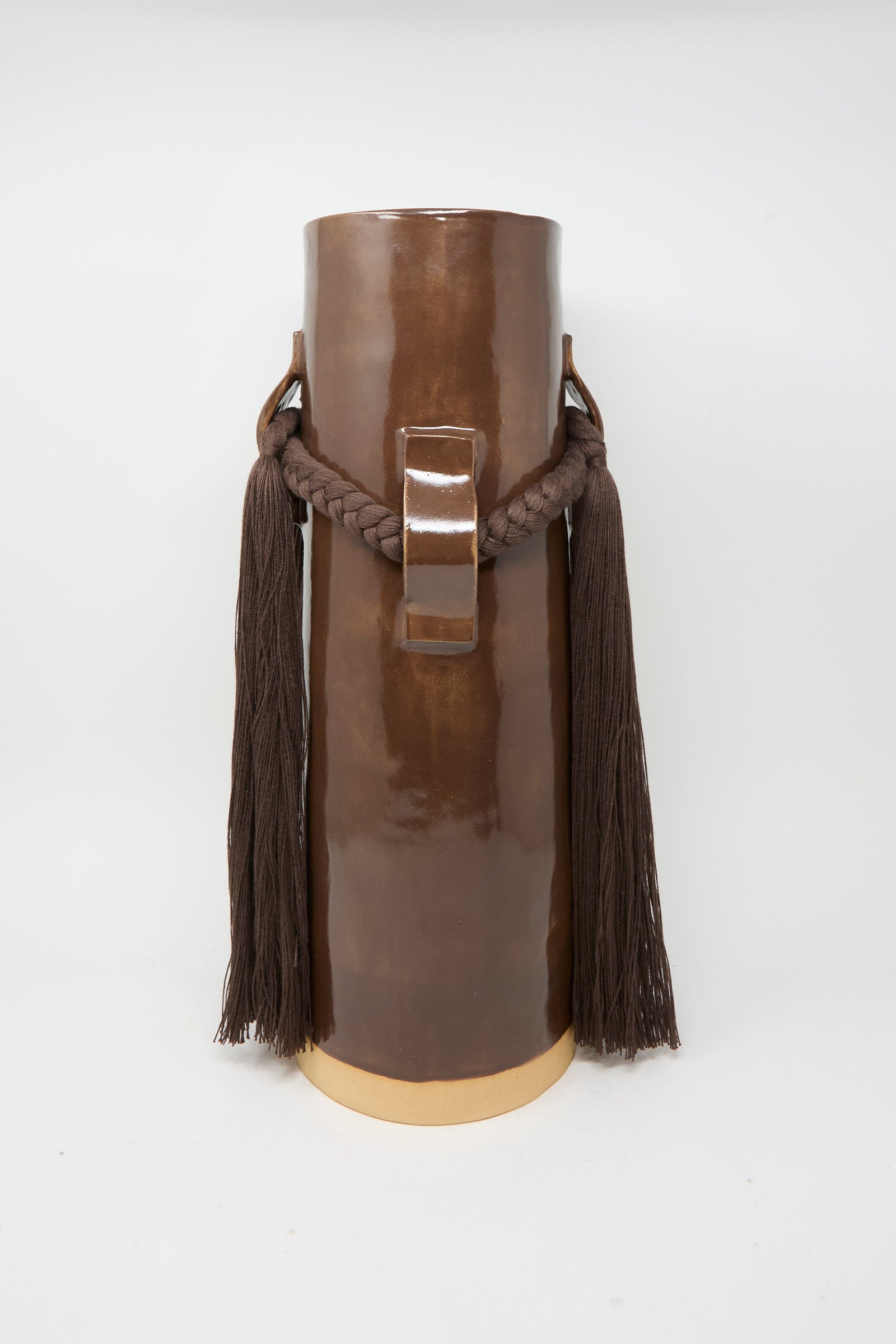 Vase #800 in Brown by Karen Tinney features a tall, glossy brown glazed form with a central handle, thick braided rope adorned with long tassels on each side, and stands on a cream-colored base—a striking example of the brand’s Vermont pottery craftsmanship.
