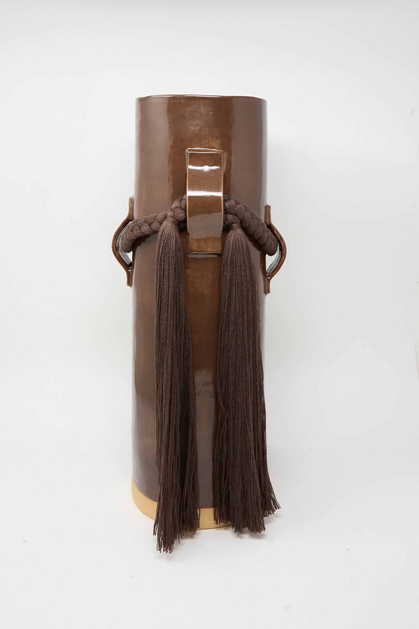 Vase #800 in Brown by Karen Tinney is a tall, cylindrical vase with a brown glaze, crafted in the tradition of Vermont pottery and featuring braided rope and long brown tassels draped over metal loops on each side.