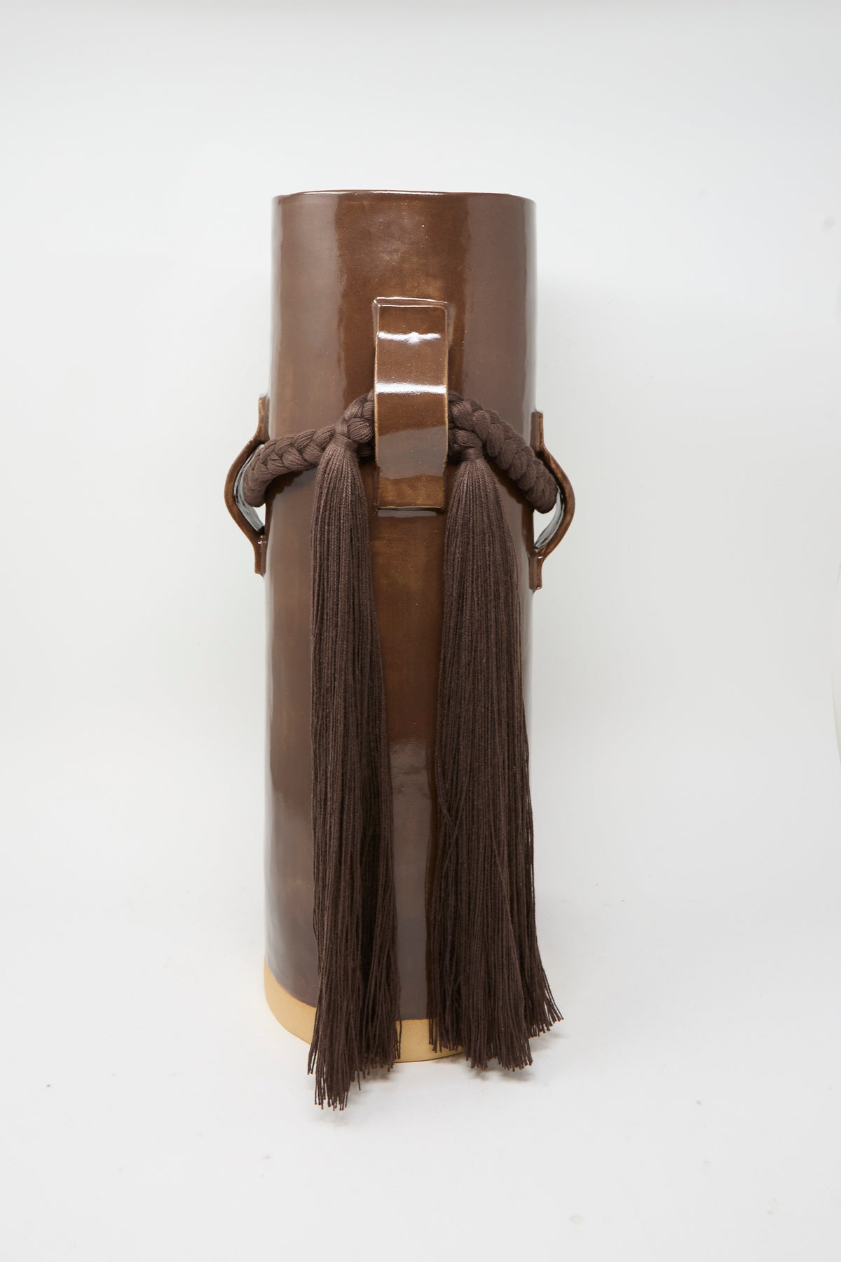 Vase #800 in Brown by Karen Tinney is a tall, cylindrical vase with a brown glaze, crafted in the tradition of Vermont pottery and featuring braided rope and long brown tassels draped over metal loops on each side.