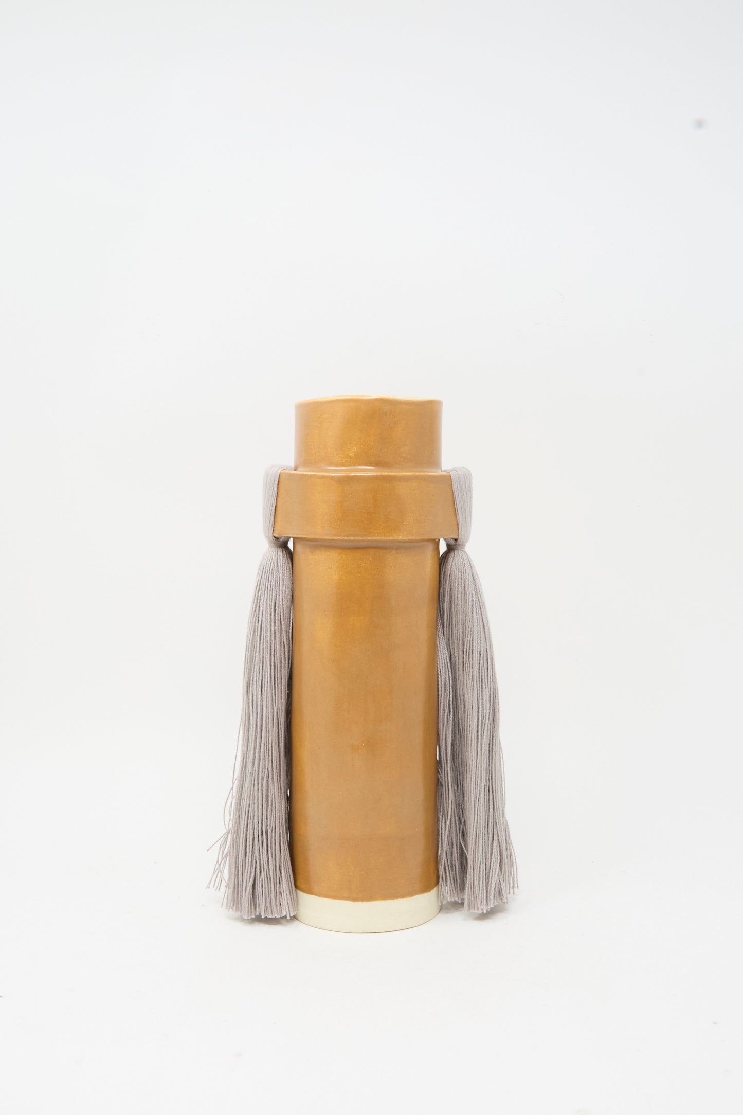 Vase #825 in Brown and Gray by Karen Tinney is a tall, cylindrical stoneware piece with a wide neck, adorned with two thick gray tassels on each side and finished in a smooth satin brown glaze, set against a plain white background.