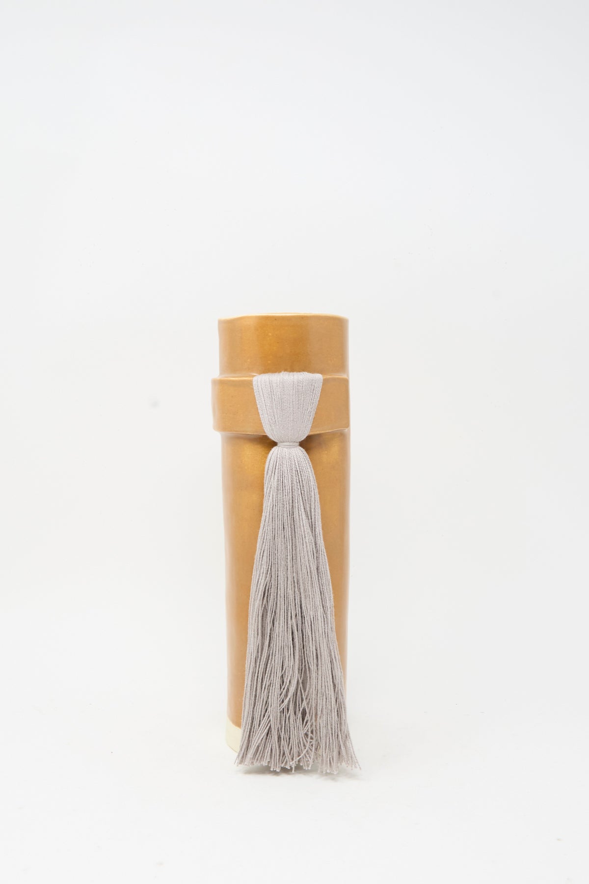 Vase #825 in Brown and Gray by Karen Tinney features a cylindrical brown leather form with a lid, adorned with a long, light gray tassel at the front—a design reminiscent of a handmade vase finished in satin brown glaze.