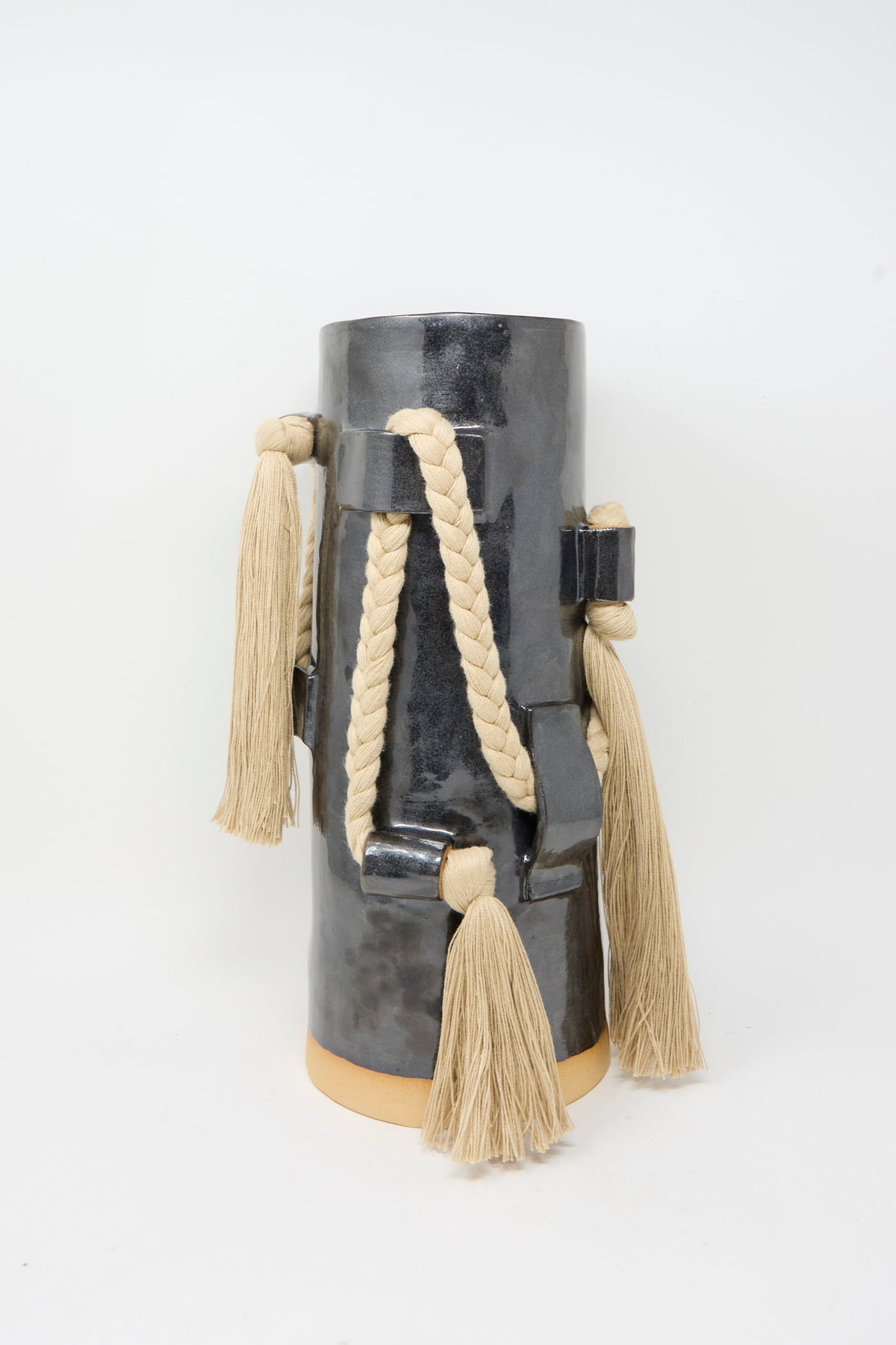 Vase #846 in Black and Tan by Karen Tinney—a tall, glossy black ceramic vase finished with a striking black glaze and adorned with beige rope and tassel decorations along its sides—displayed against a plain white background.