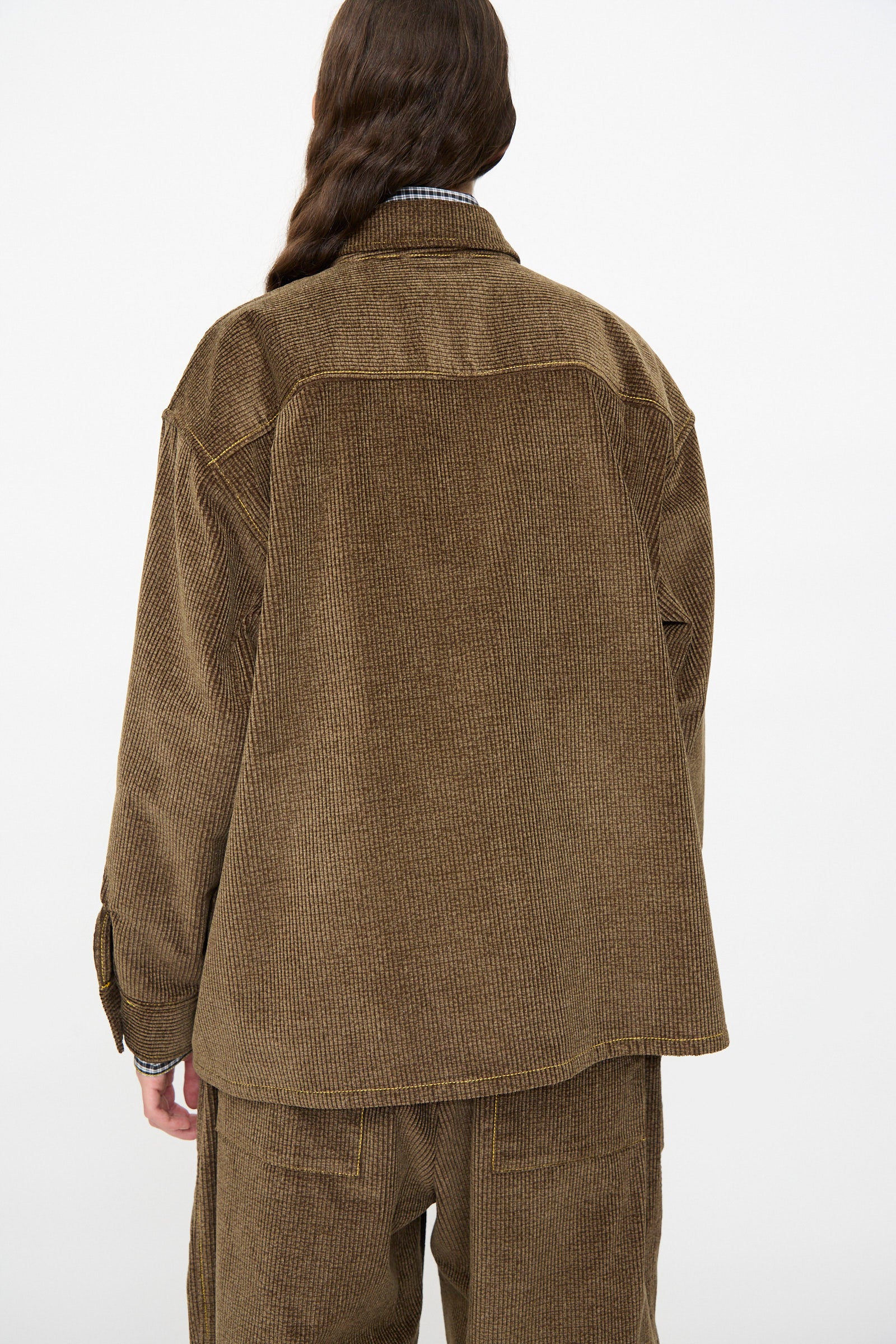 A model is shown from the back wearing the KasMaria Corduroy Oversized Shirt Jacket in Brown, crafted from soft Japanese cotton, against a plain white background.