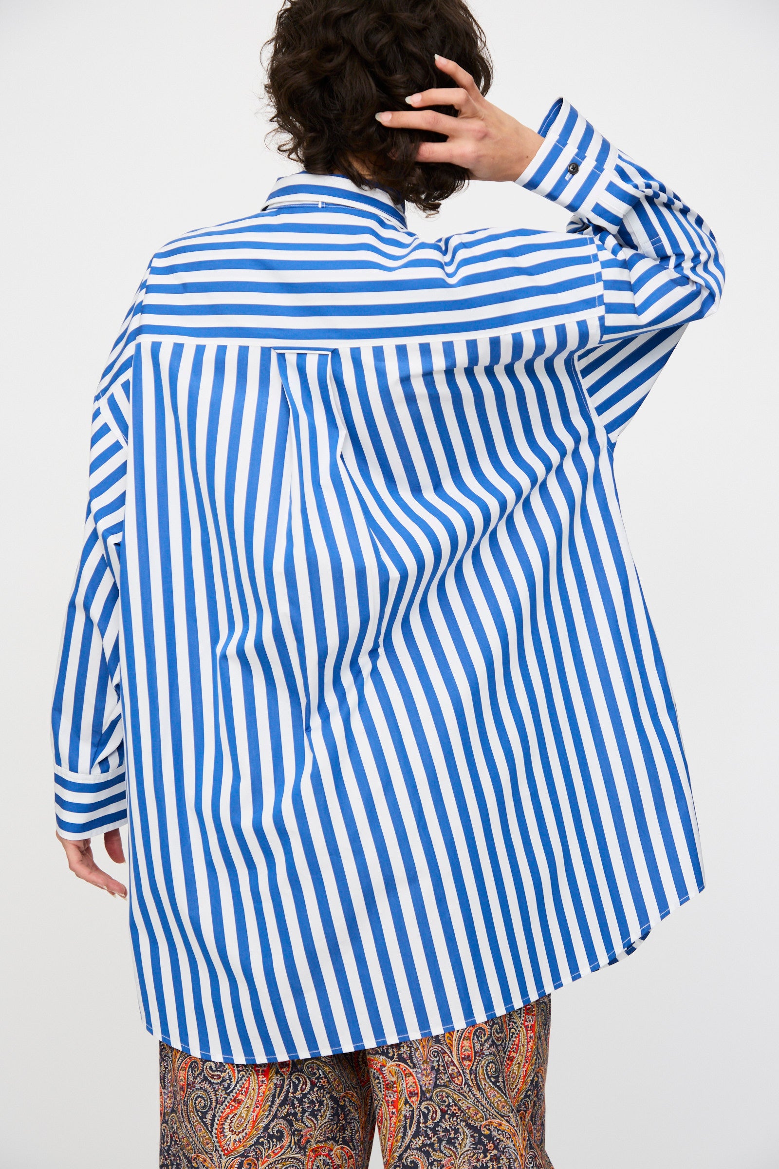Person facing away, wearing the KasMaria Cotton Poplin Oversized Dress with Tie in Stripe, one hand touching the back of their head.