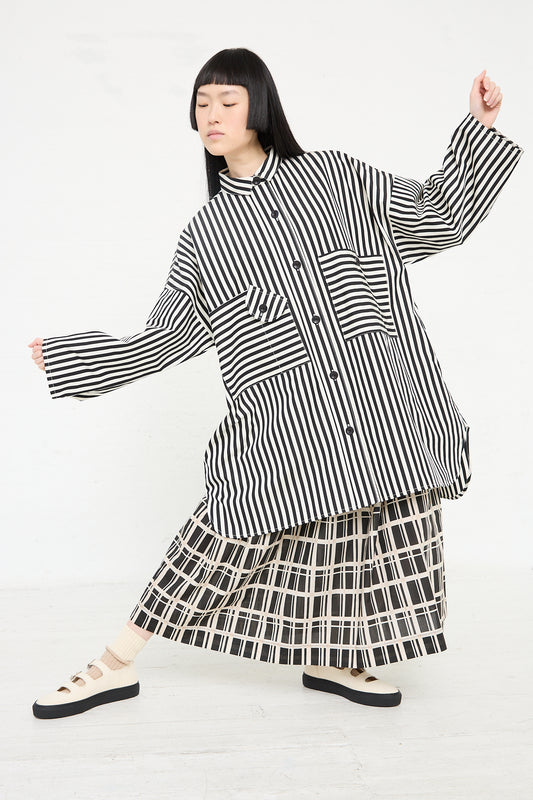 A woman in a playful KasMaria Cotton Poplin Oversized Smock Dress in Stripe and relaxed fit skirt ensemble posing on a white background.
