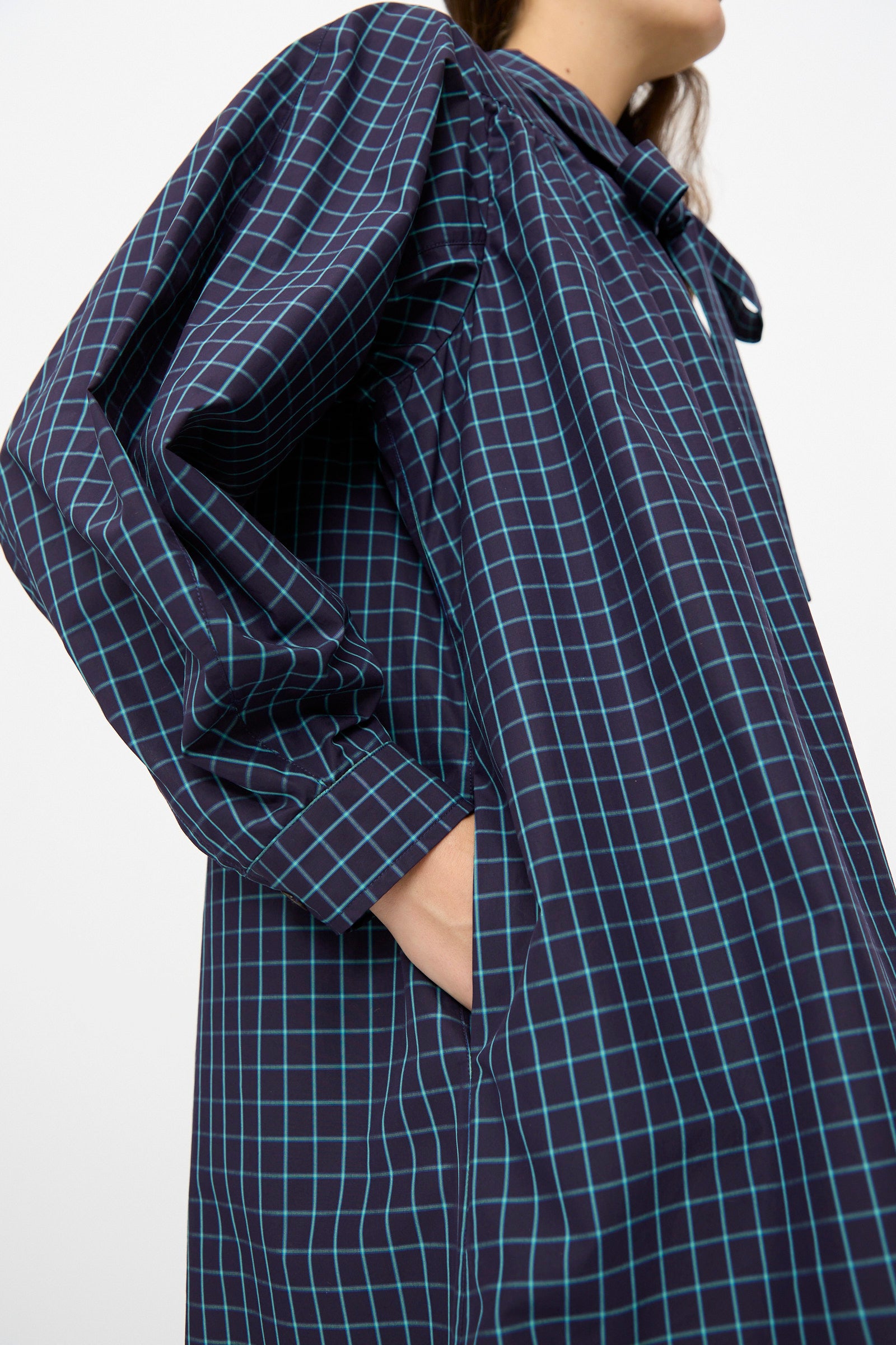 A person wears the KasMaria Cotton Poplin Smock Dress in Blue Check—an oversized navy Italian cotton poplin dress with a light blue check grid, standing with one hand in a side pocket.