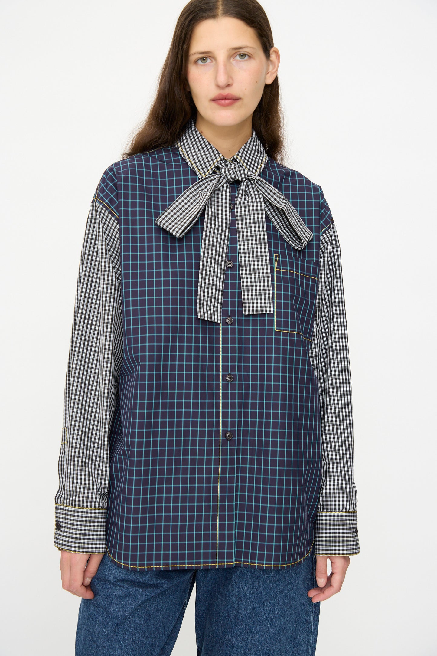 A person wears the KasMaria Cotton Shirt with Tie in Check Combo, featuring a relaxed fit, contrasting checked sleeves, and a large bow tie collar, standing against a plain background.