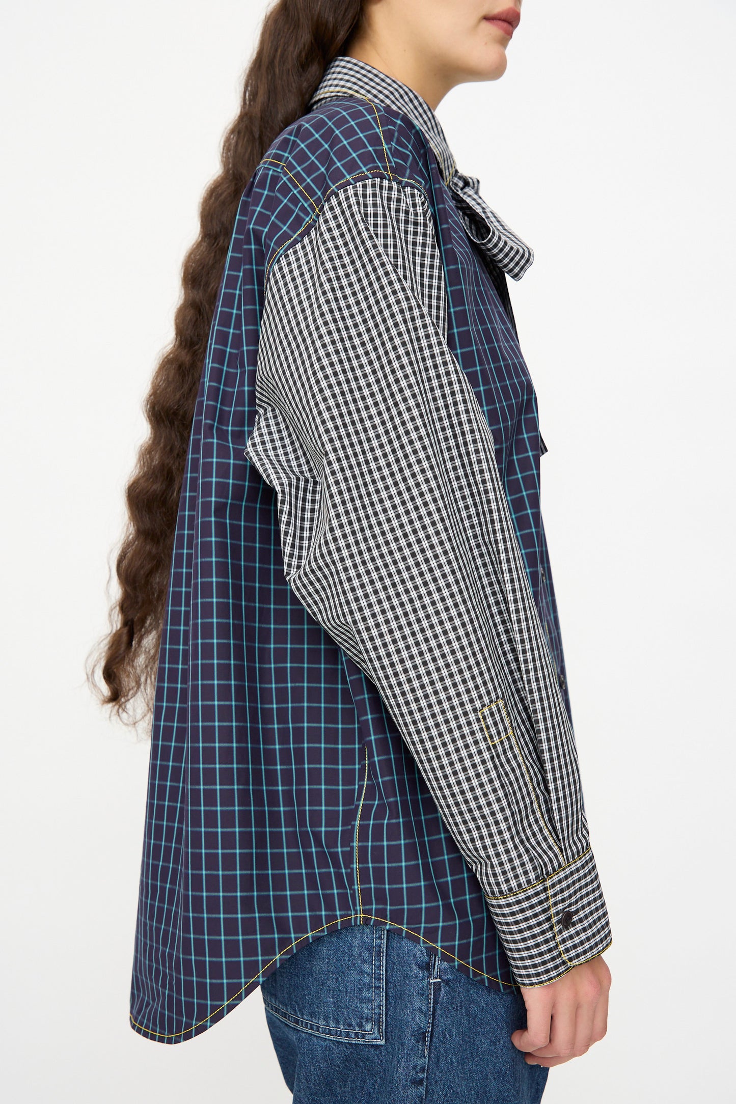 A person is seen from the side wearing the KasMaria Cotton Shirt with Tie in Check Combo, a relaxed-fit, long-sleeve button-down featuring mixed check and plaid patterns, paired with blue jeans.
