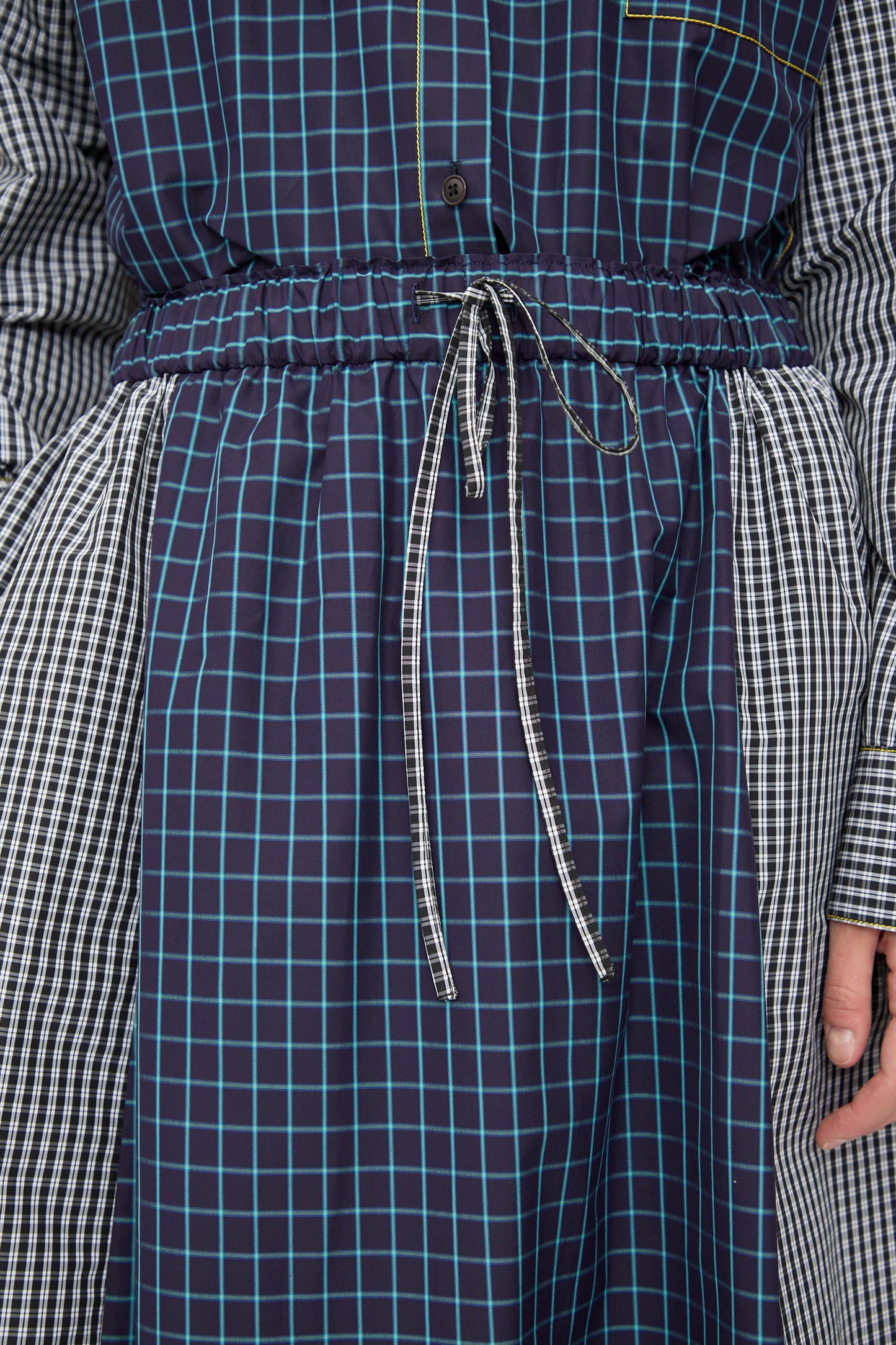 Close-up of a person wearing the KasMaria Cotton Skirt in Check Combo, crafted from Italian cotton with blue, white, and black checkered and plaid patterns, featuring a drawstring tie at the cinched waist.