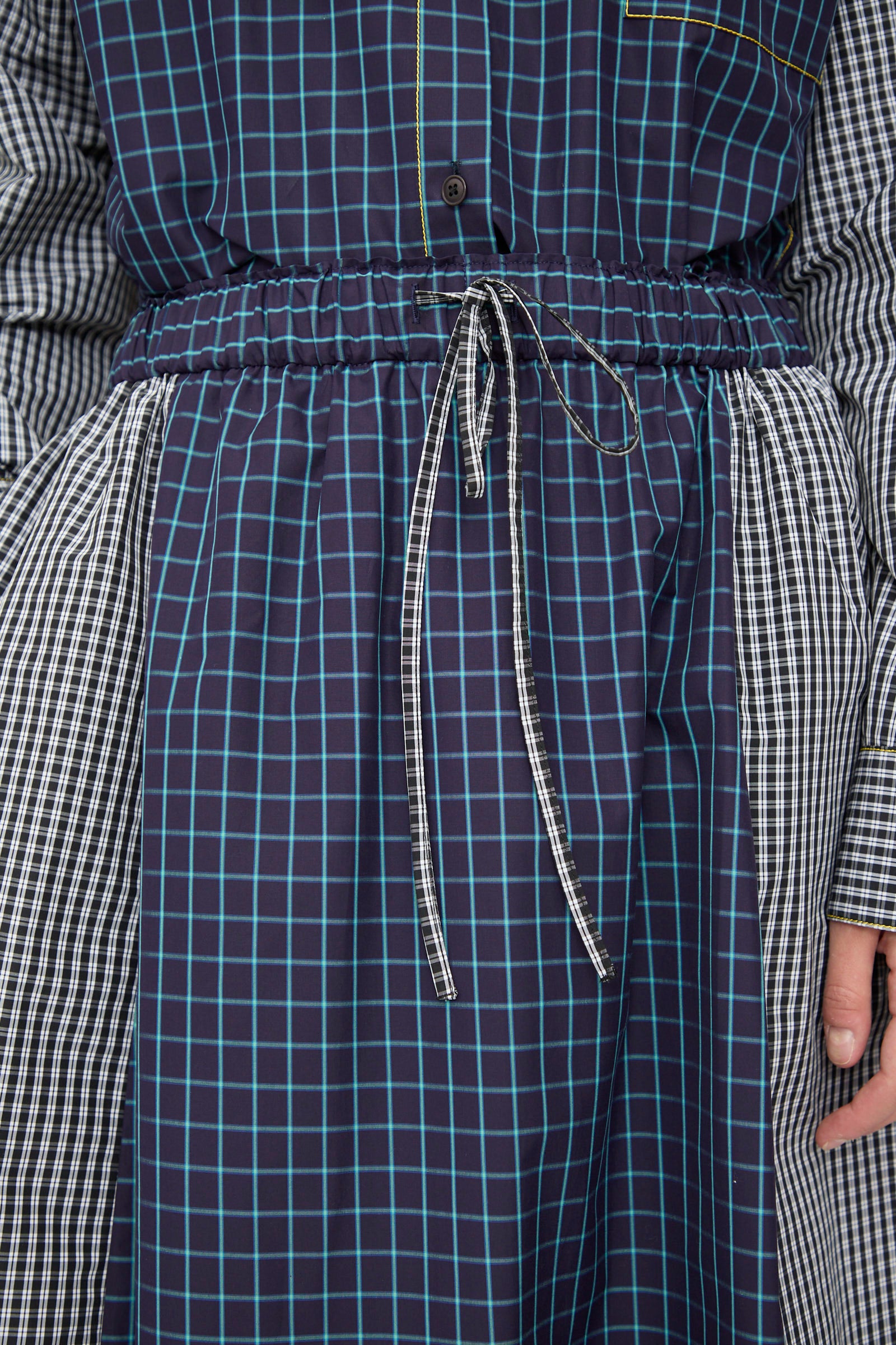 Close-up of a person wearing the KasMaria Cotton Skirt in Check Combo, crafted from Italian cotton with blue, white, and black checkered and plaid patterns, featuring a drawstring tie at the cinched waist.