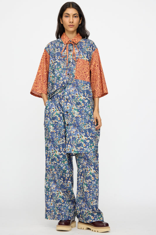 A person faces forward wearing KasMaria’s Liberty Floral Baggy Pleated Trouser in Blue, made from Liberty of London Tana Lawn Cotton, styled with a patterned shirt and chunky beige shoes—an NYC-made ensemble.