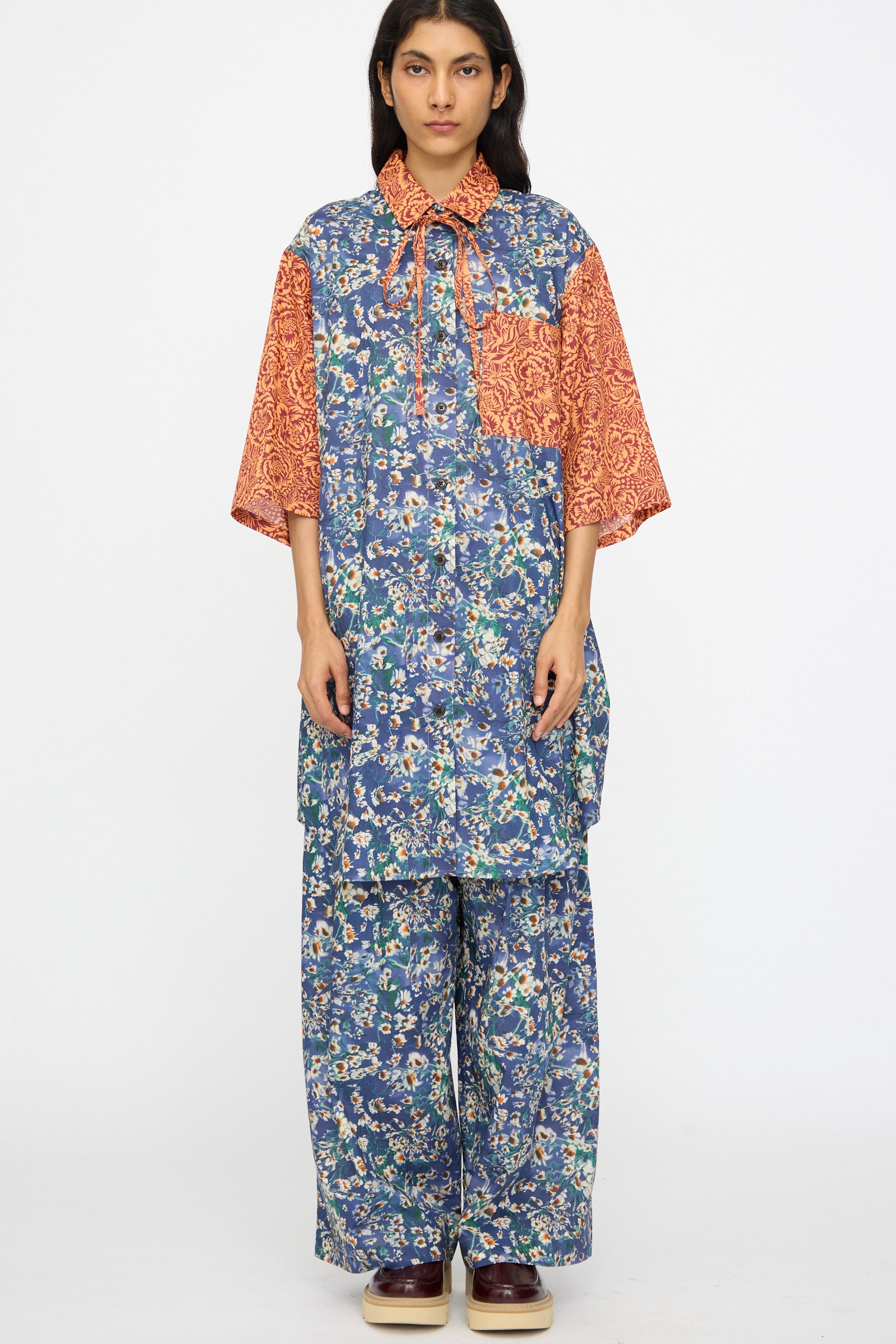 A person stands against a white background wearing the KasMaria Liberty Floral Oversized Shirtdress in Blue and Orange.