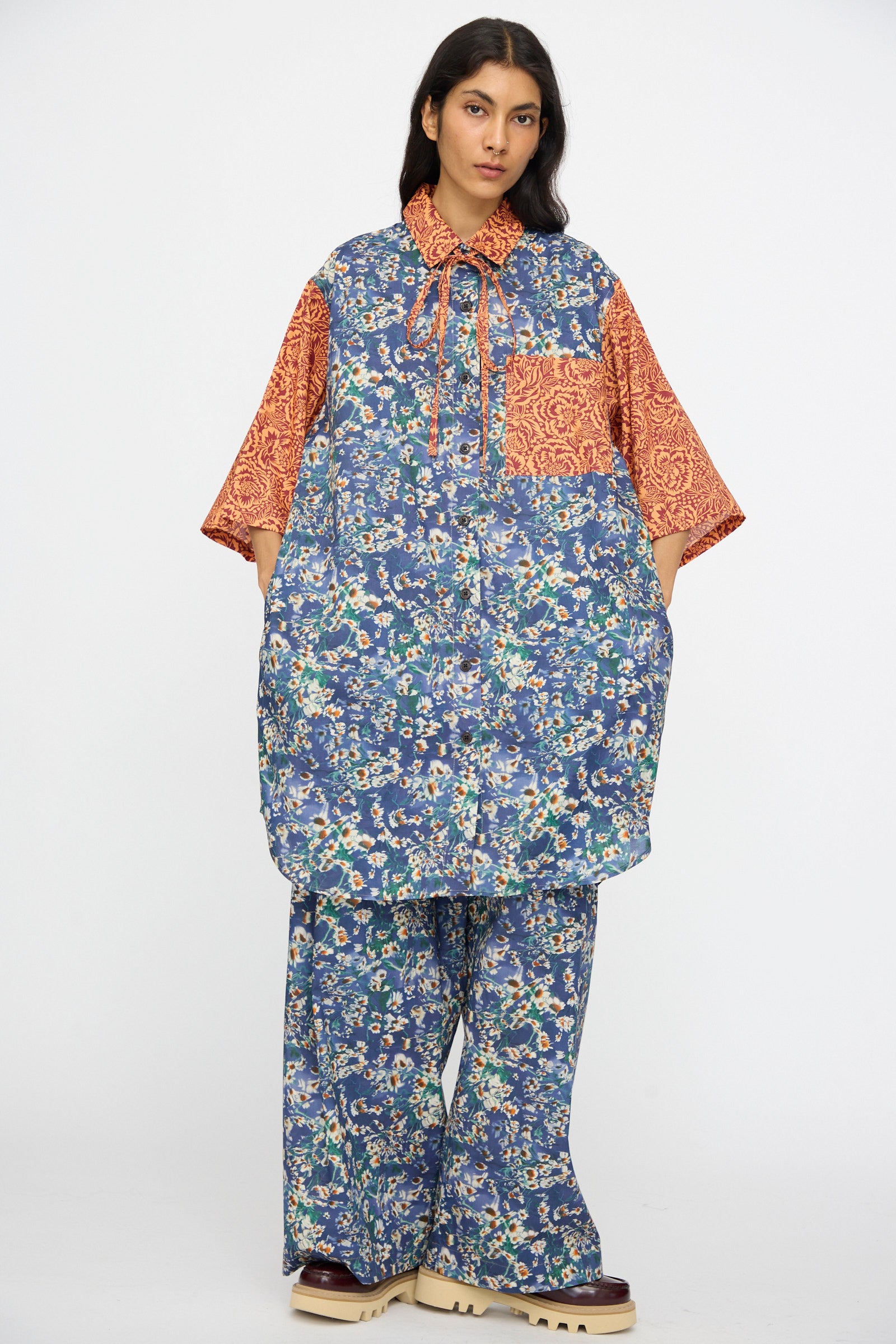 A person wears the KasMaria Liberty Floral Oversized Shirtdress in Blue and Orange, featuring mixed patterns, paired with beige platform shoes.