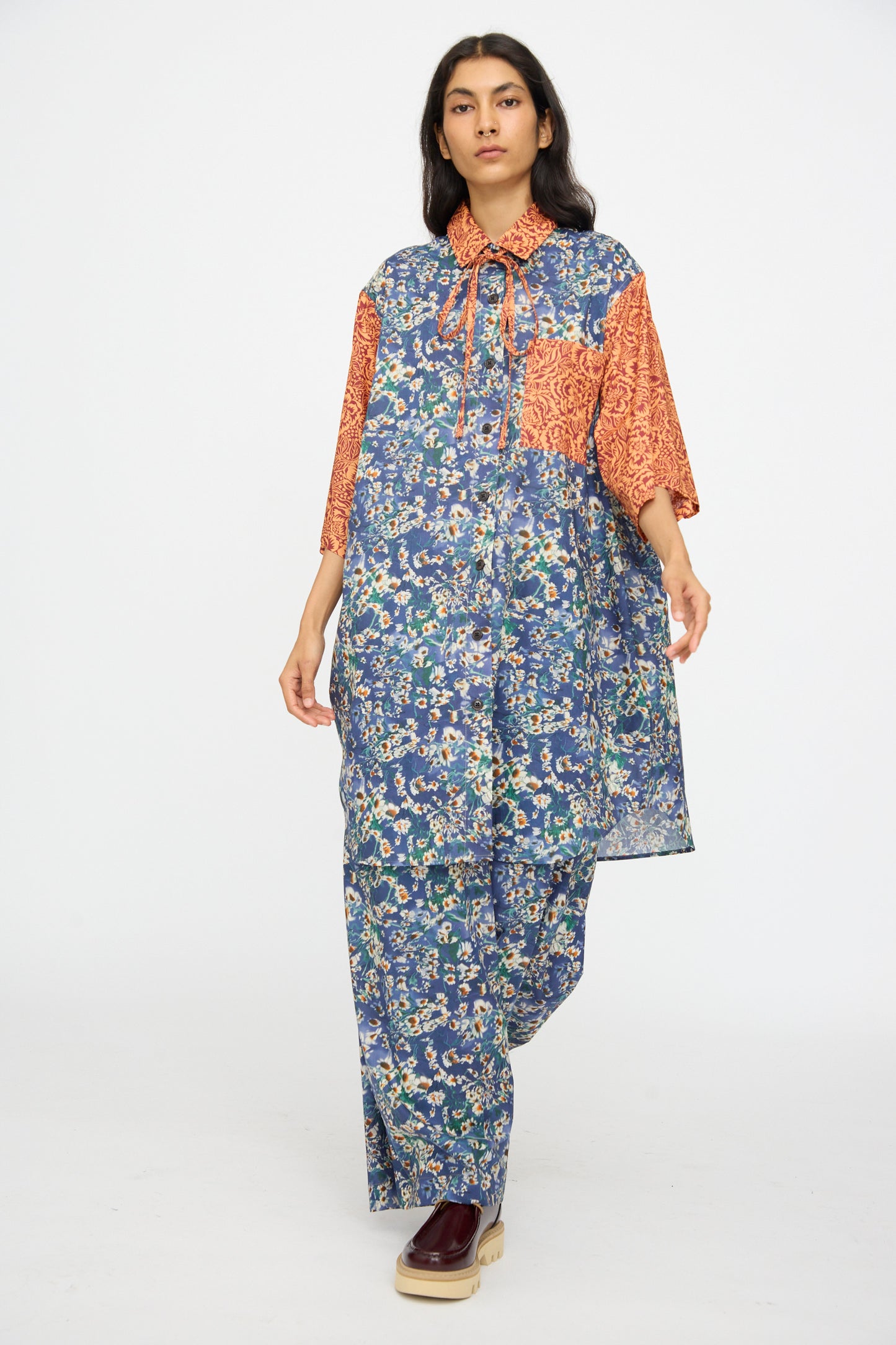 A model in the KasMaria Liberty Floral Oversized Shirtdress in Blue and Orange walks toward the camera against a plain background, paired with maroon platform shoes.