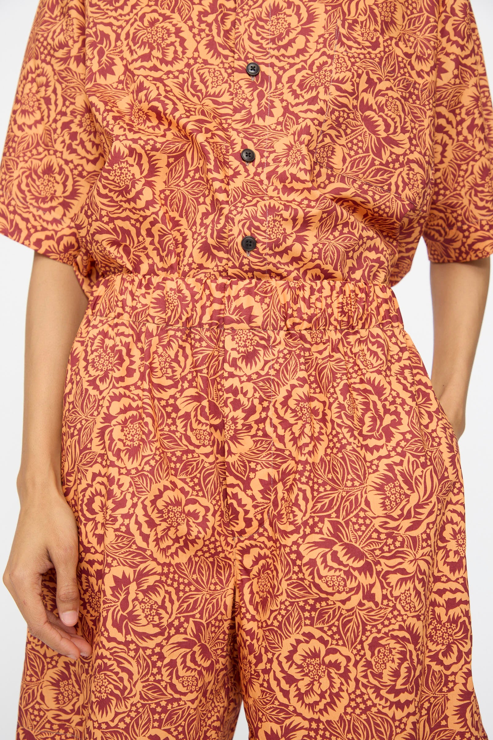 A person wears KasMaria's Liberty Floral Shorts in Orange, made from Liberty of London Tana Lawn Cotton; only the torso and upper legs are visible.