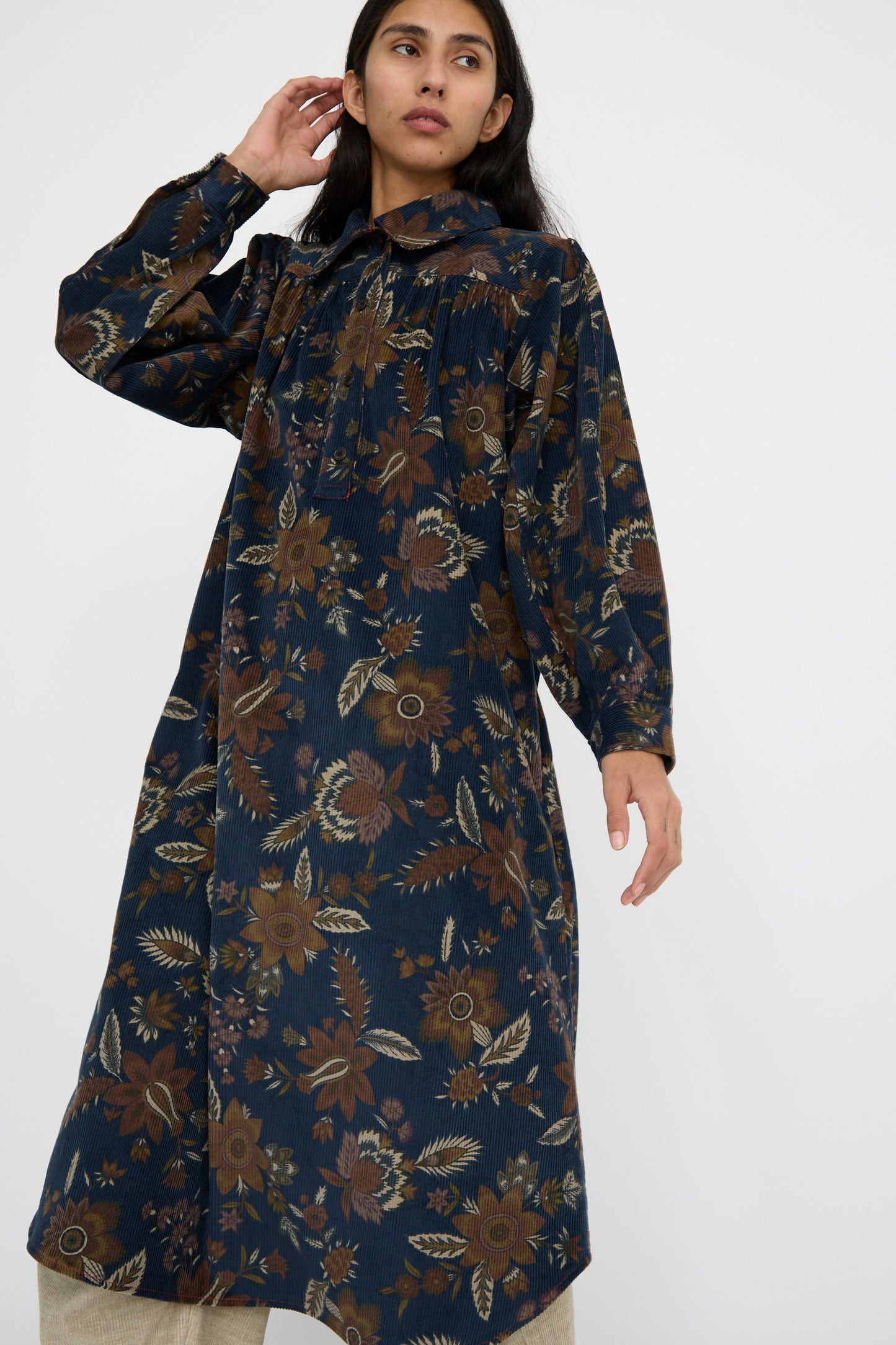 A person poses in the Corduroy Dress in Printed Floral by KasMaria, featuring long sleeves and a Japanese floral design, made entirely from 100% cotton, against a plain background.