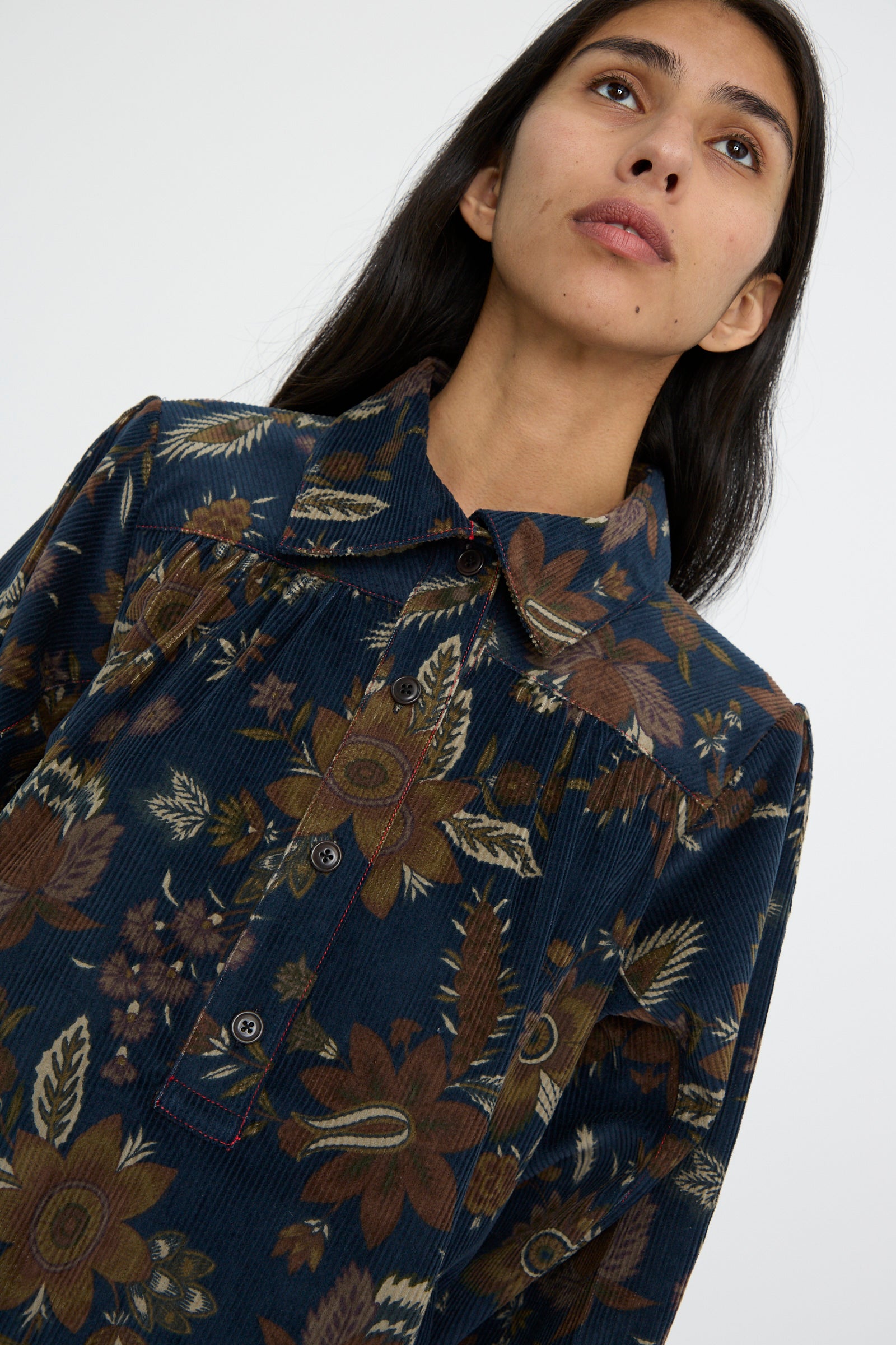 A person with long dark hair is wearing the Corduroy Dress in Printed Floral by KasMaria, featuring a Japanese floral pattern and crafted from 100% cotton, against a white background. 