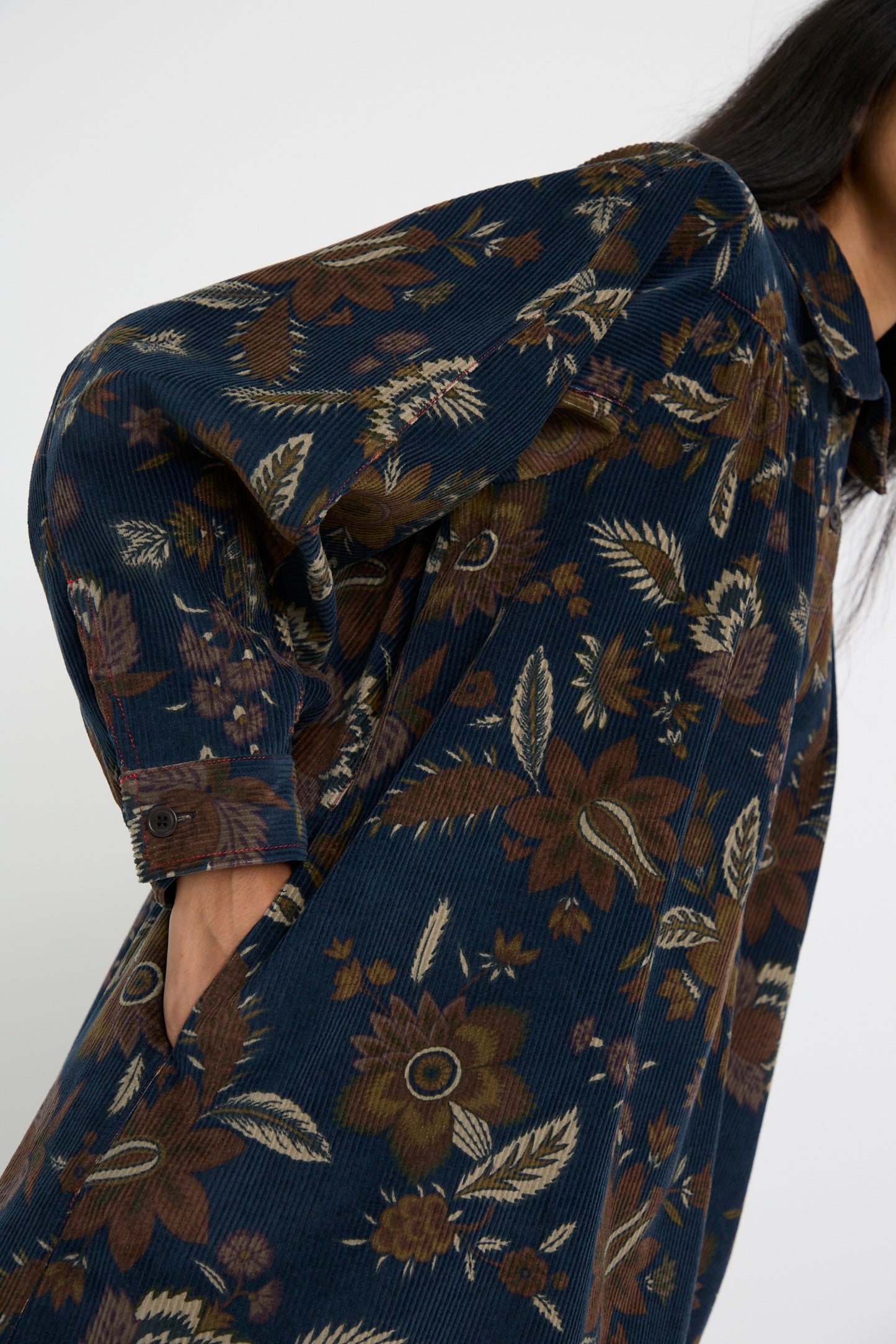 A person wearing a KasMaria Corduroy Dress in Printed Floral, with their hand in a side pocket, against a white background. 