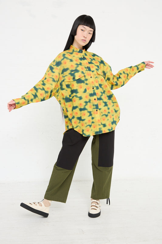 A person posing in a playful wearables KasMaria Cotton Linen Large Front Pocket Shirt in Daffodil Print and contrasting pants against a plain background.