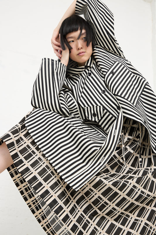 A person with a striking black hairstyle poses in an KasMaria Cotton Pleated Long Skirt in Grid Print and a black and white striped shirt against a white background.