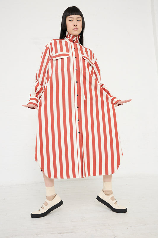 Woman posing in a KasMaria Cotton Poplin Ruffle Neck Shirt Dress in Stripe with a high collar and playful ruffle detail, paired with socks and sandals.