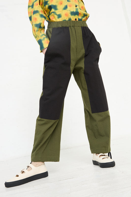 Person wearing the KasMaria Cotton Seersucker Work Pant in Combo Color, a relaxed fit pant with color-blocked green and black panels, paired with white shoes with black details, standing against a white background.