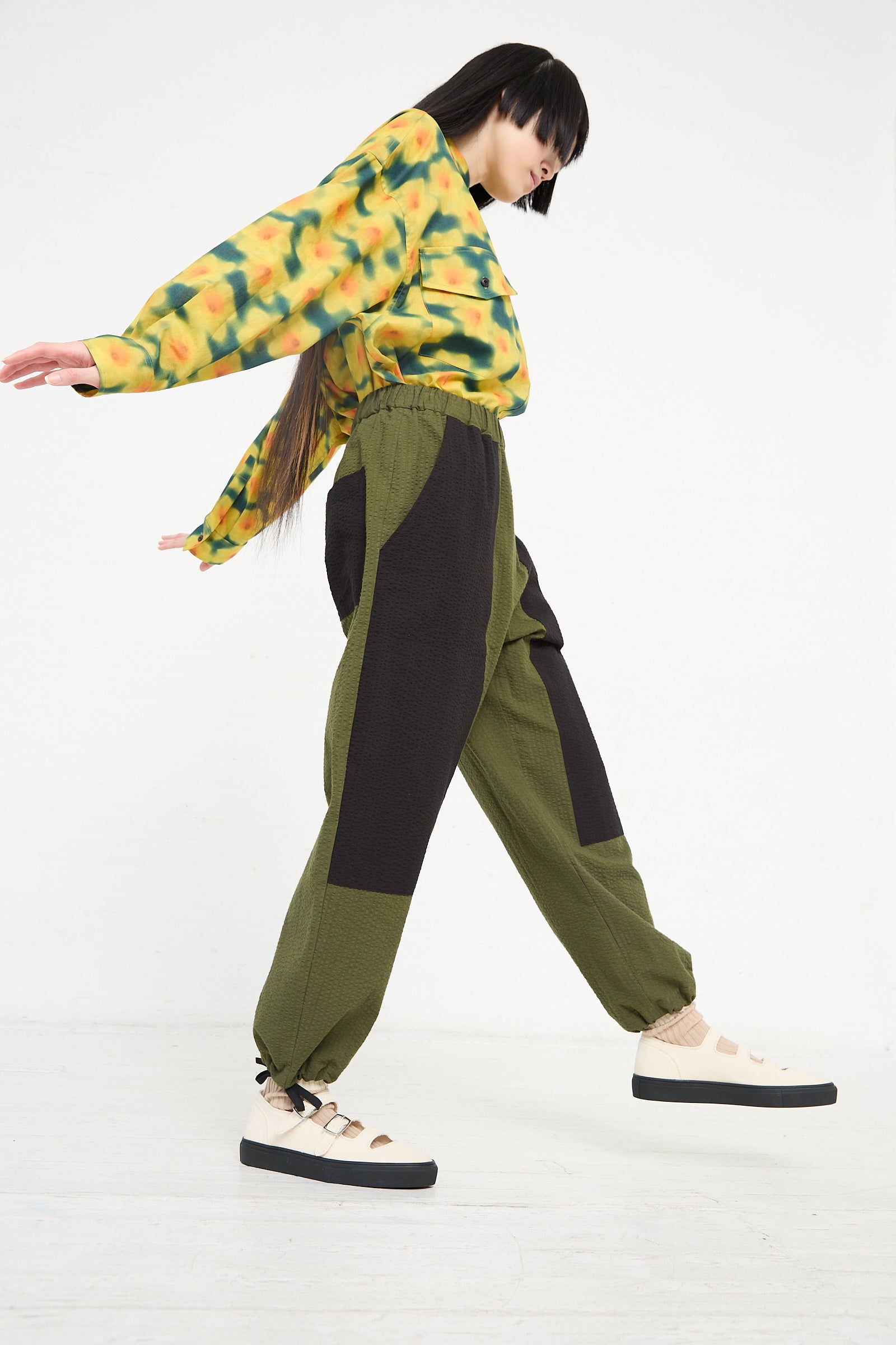 Woman in colorful top and relaxed fit KasMaria Cotton Seersucker Work Pant in Combo Color posing mid-step against a white background.