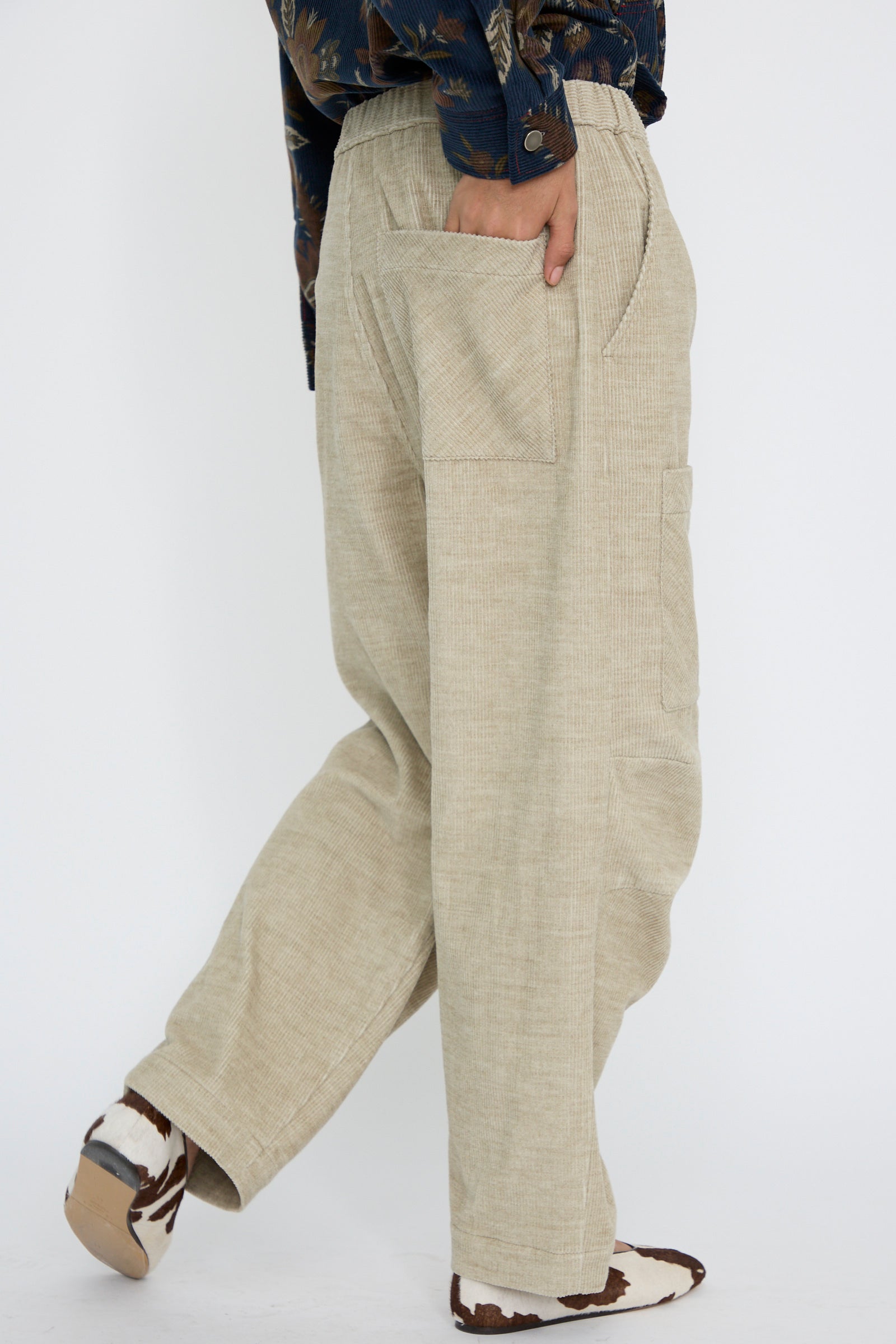 A person wearing KasMaria's Cotton Wool Corduroy Pant with Front Patch, which features an elasticated waist, and patterned shoes, casually placing one hand in a back pocket.