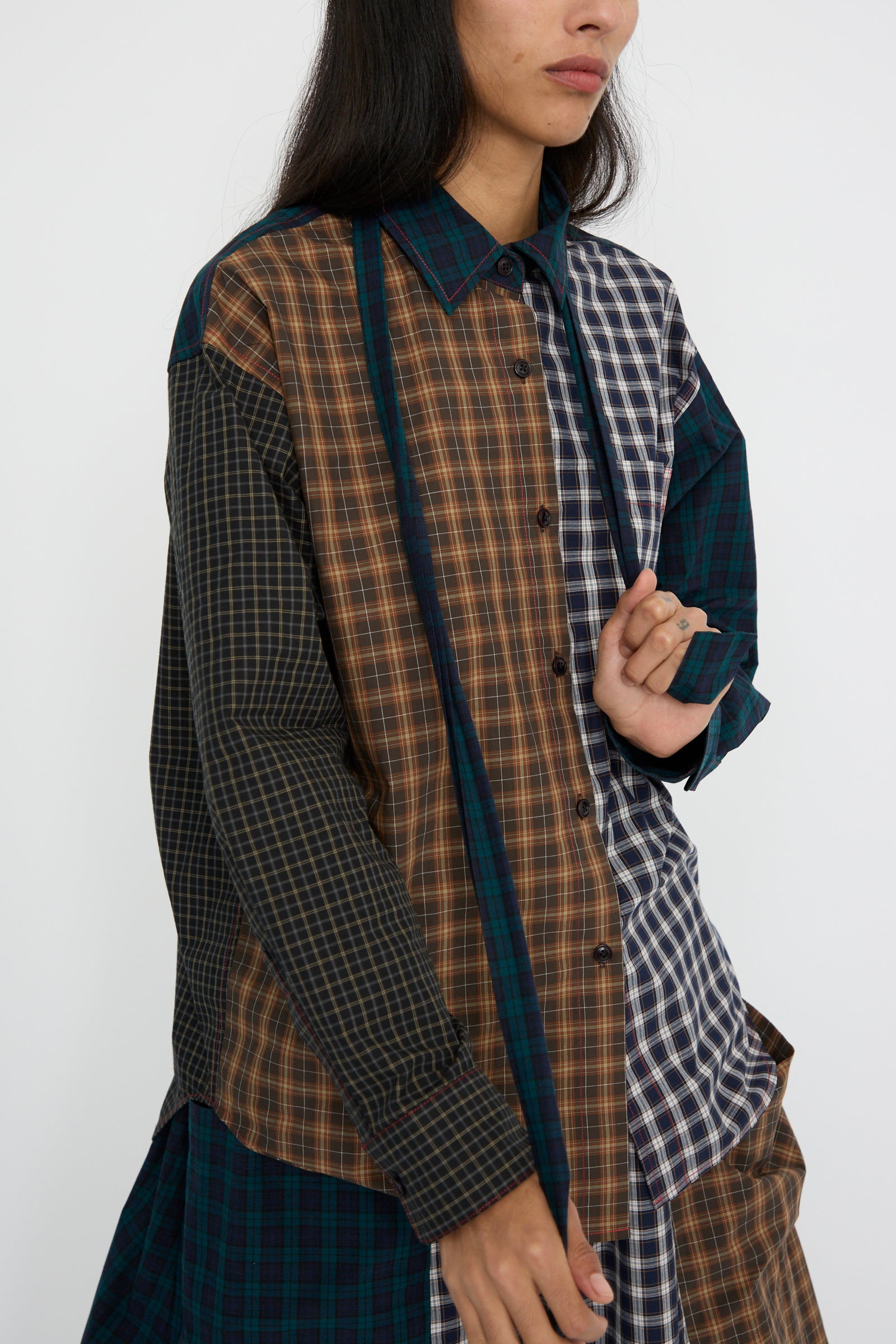 Against a plain background, a person is dressed in the KasMaria Heavy Poplin Oversized Shirt with Tie in Mixed Plaid and holding the tie. 