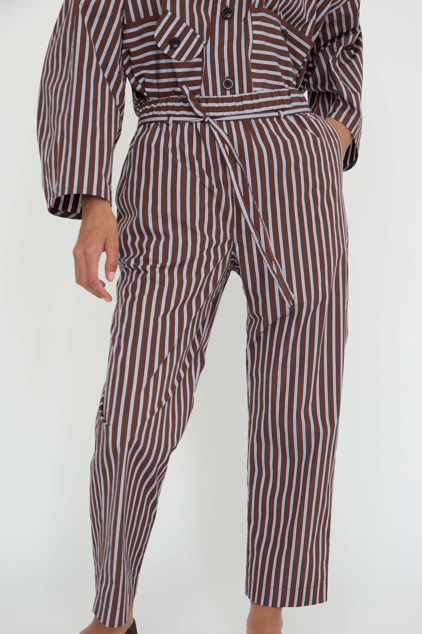 A person wearing KasMaria's Taffeta Pajama Pants with Tie in Stripe, made from Italian cotton taffeta, showcases a relaxed fit while their left hand rests in the pocket.