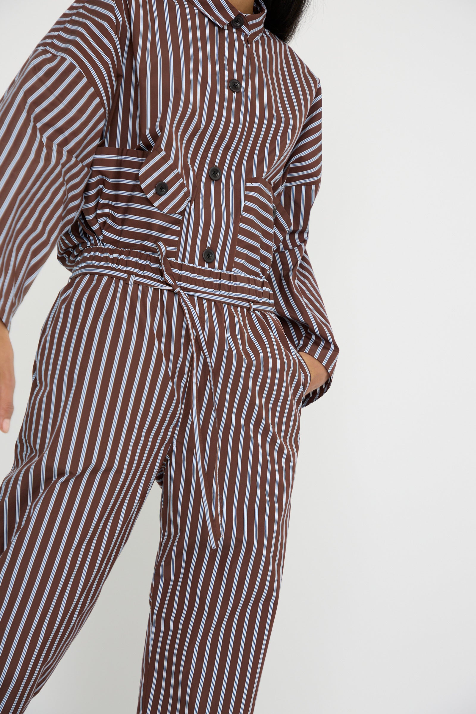 An angled shot of a person wearing the Taffeta Pajama Pants with Tie in Stripe from KasMaria, which features  a relaxed fit in brown and white striped Italian cotton taffeta. 