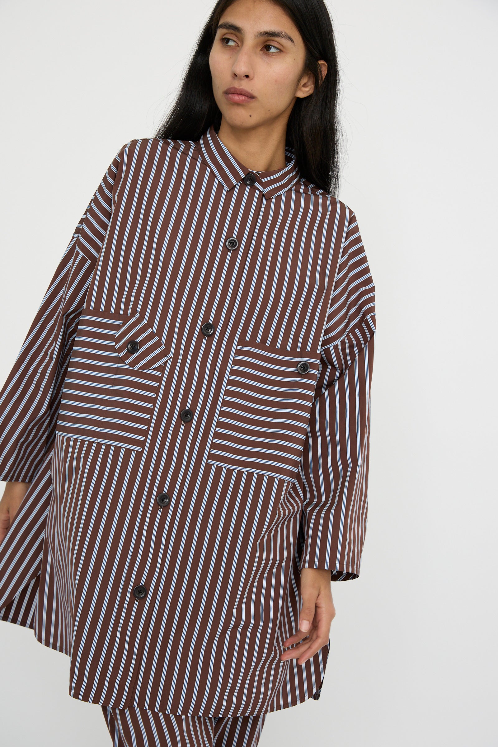 Person wearing the KasMaria Taffeta Smock Shirt Dress in Stripe, featuring an oversized fit and large pockets, looking to the side.